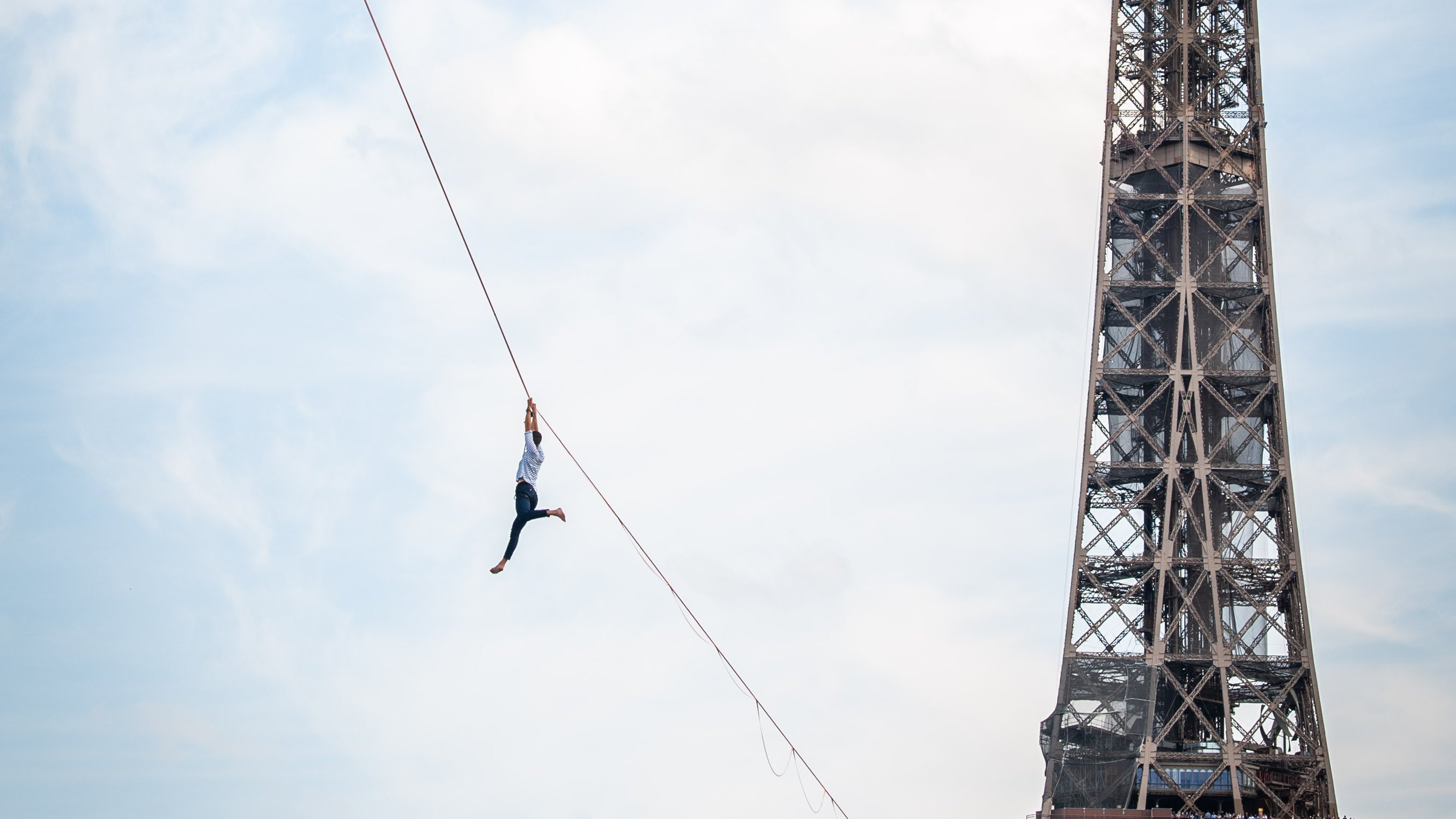 A tightrope walker hanging on a tightrope, next to the Eiffel Tower