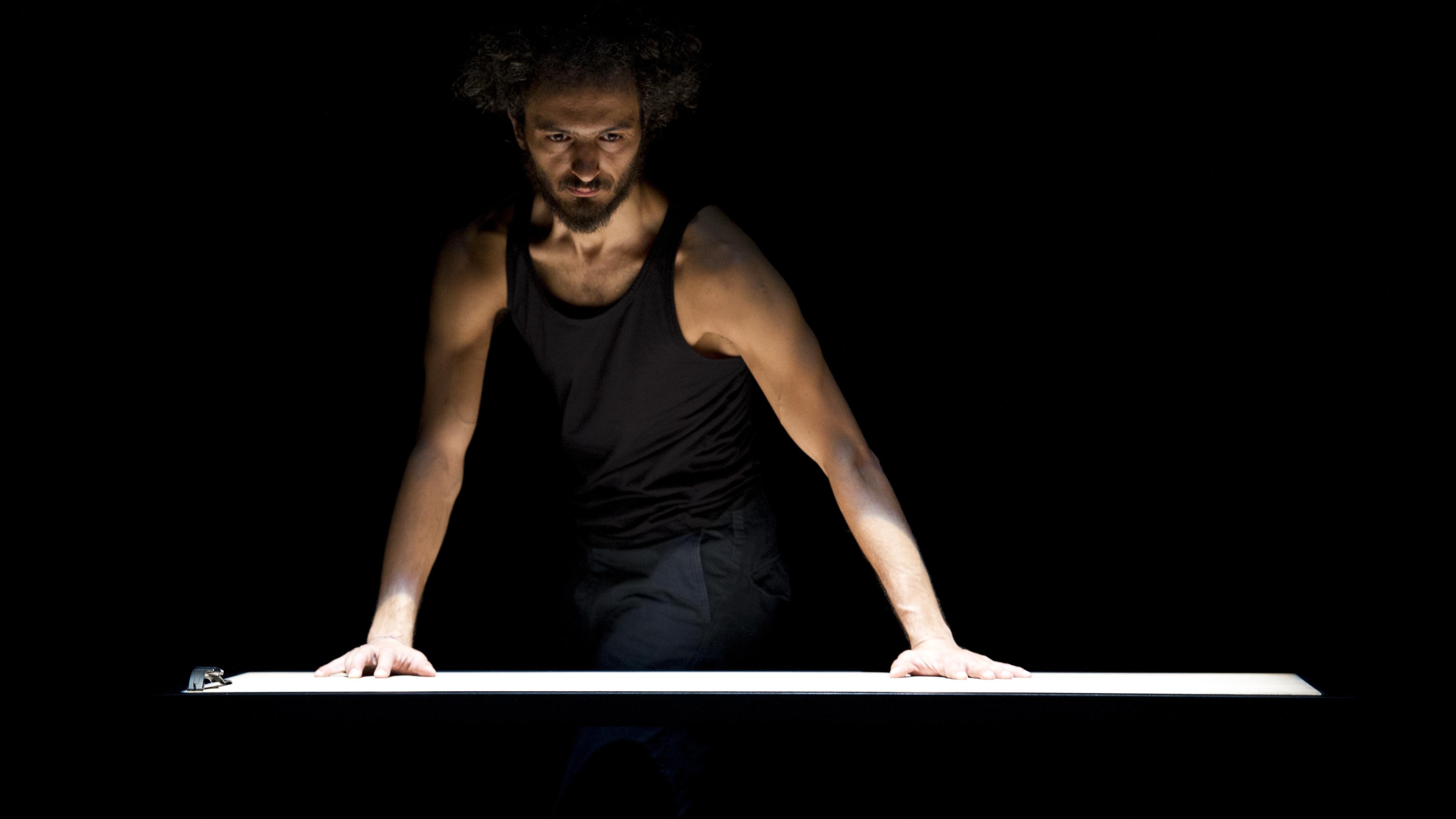 A man in a black tank top with his hands on a white table