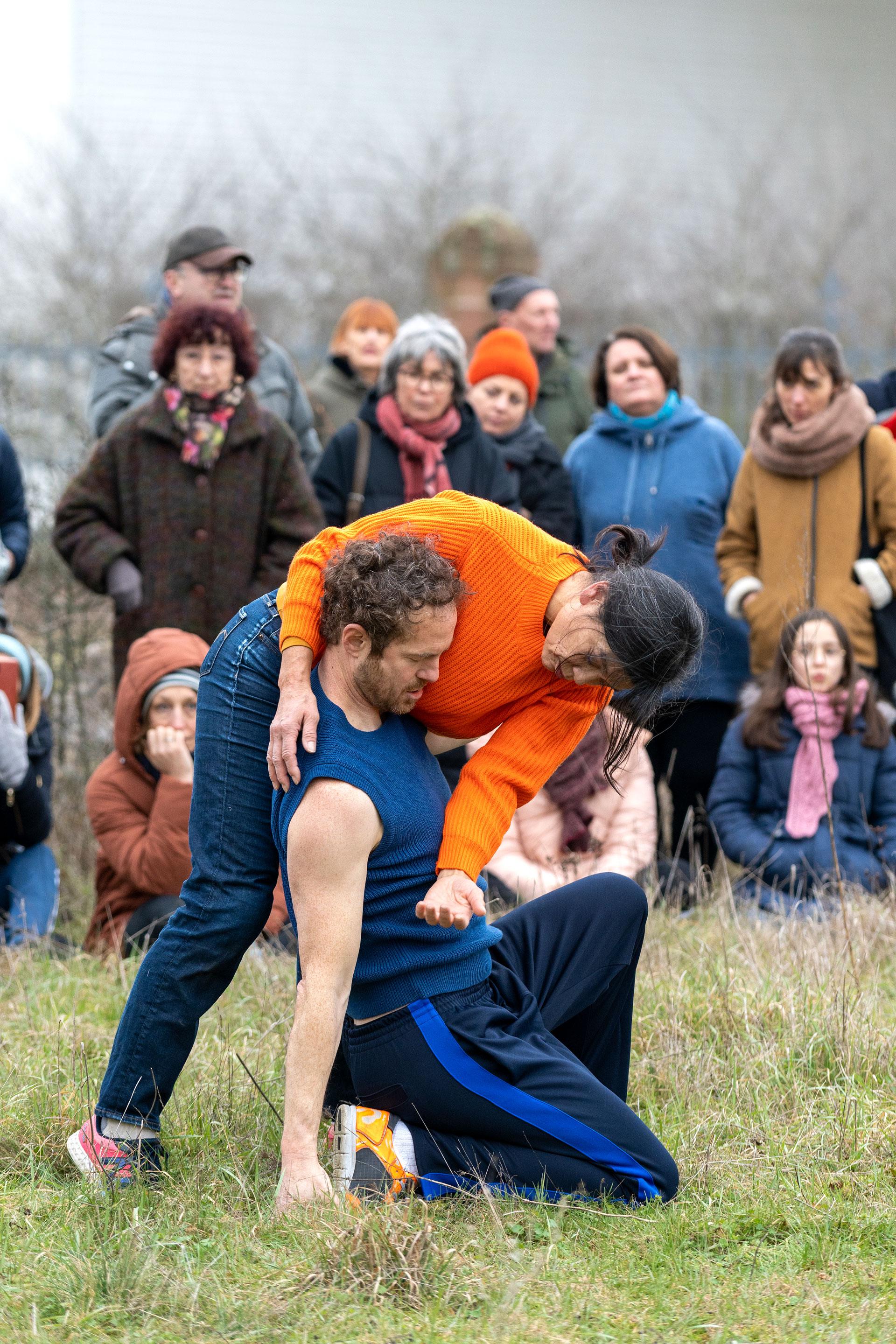 Boris Charmatz accroupi sur le sol, entouré par une danseuse avec un pull orange. 