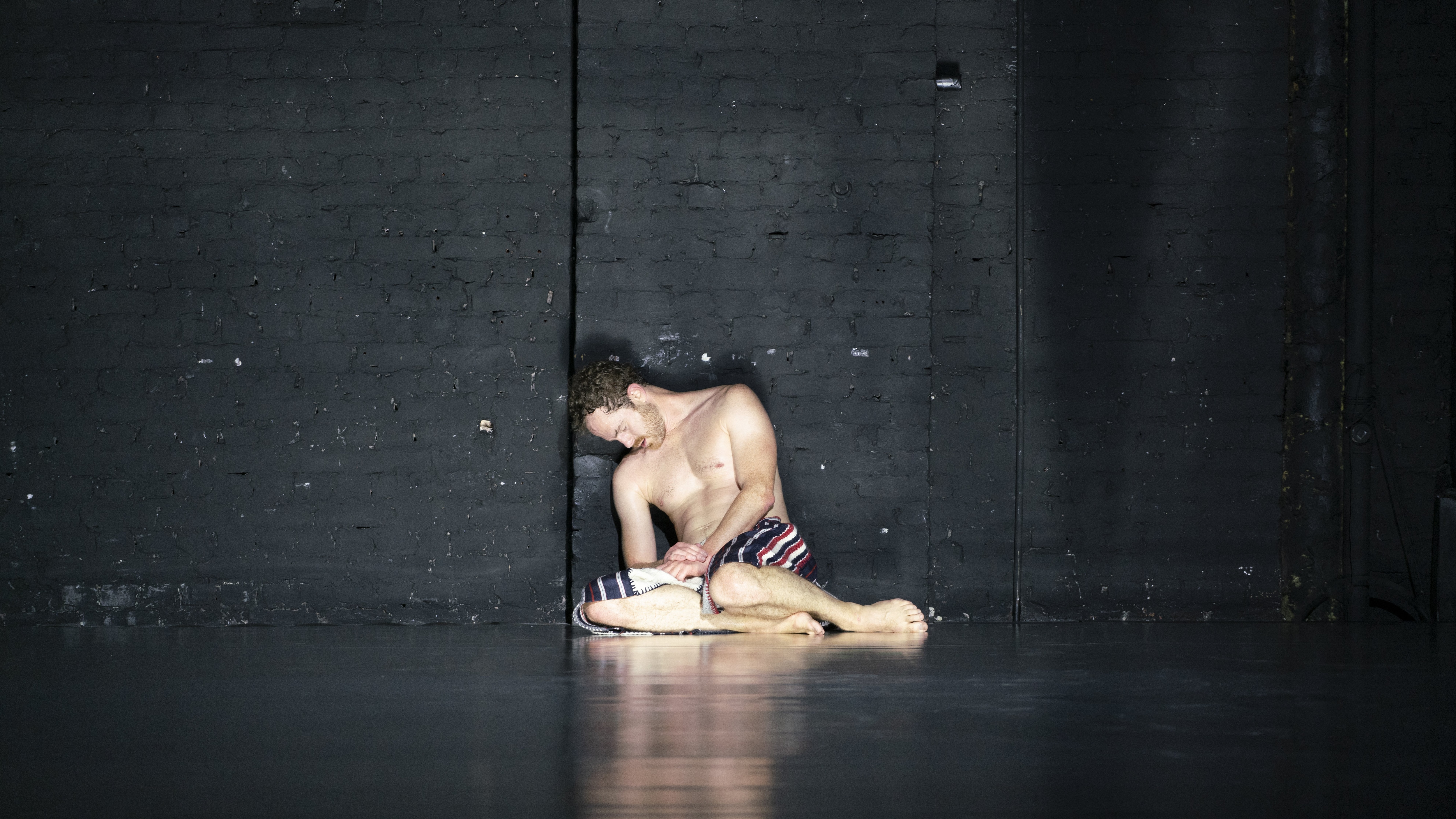 Boris Charmatz bare chested, huddled against a wall 