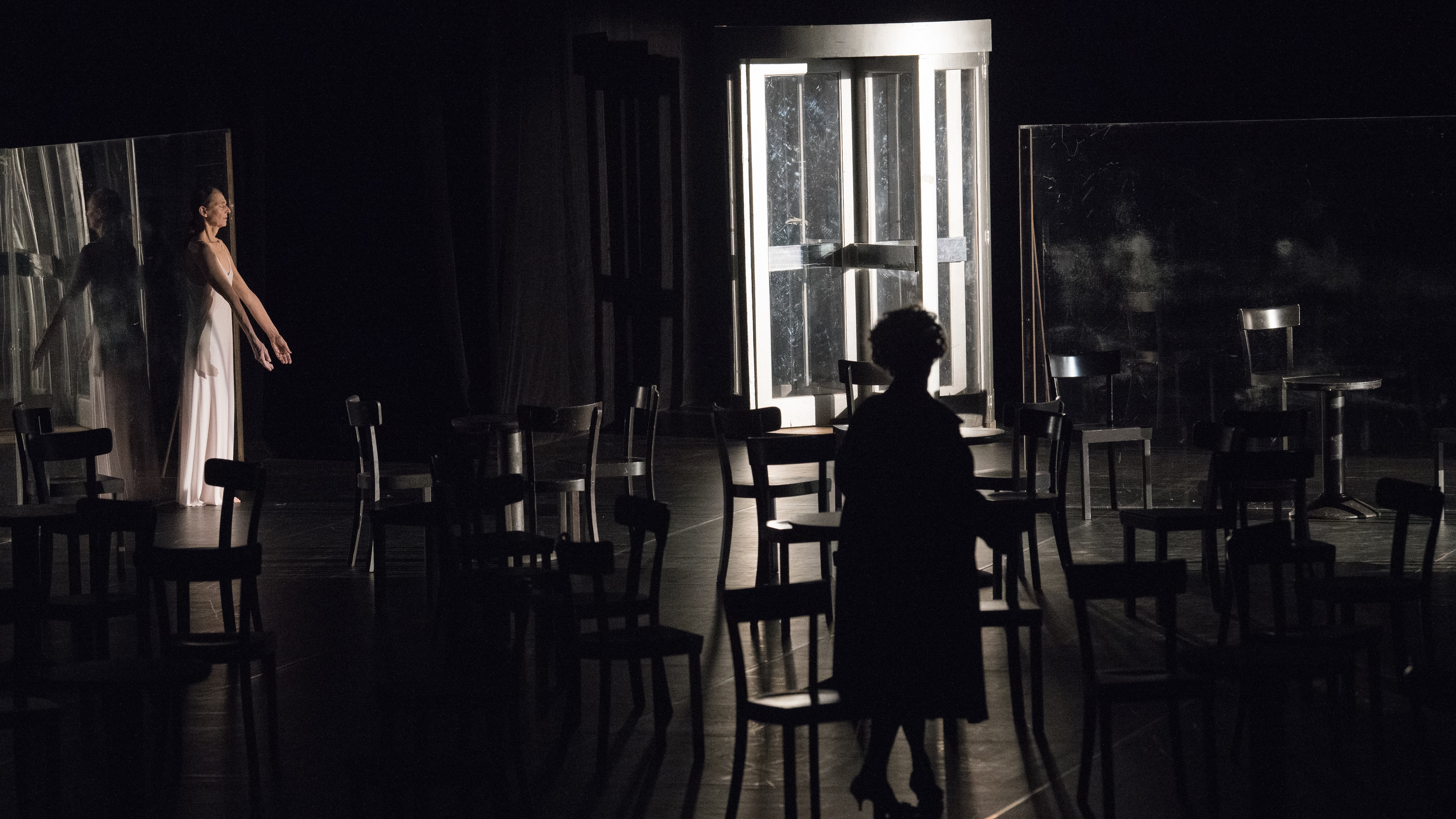 Héléna Pikon is at the back of a stage that is filled with empty chairs, her eyes are closed and her arms stretched downwards.