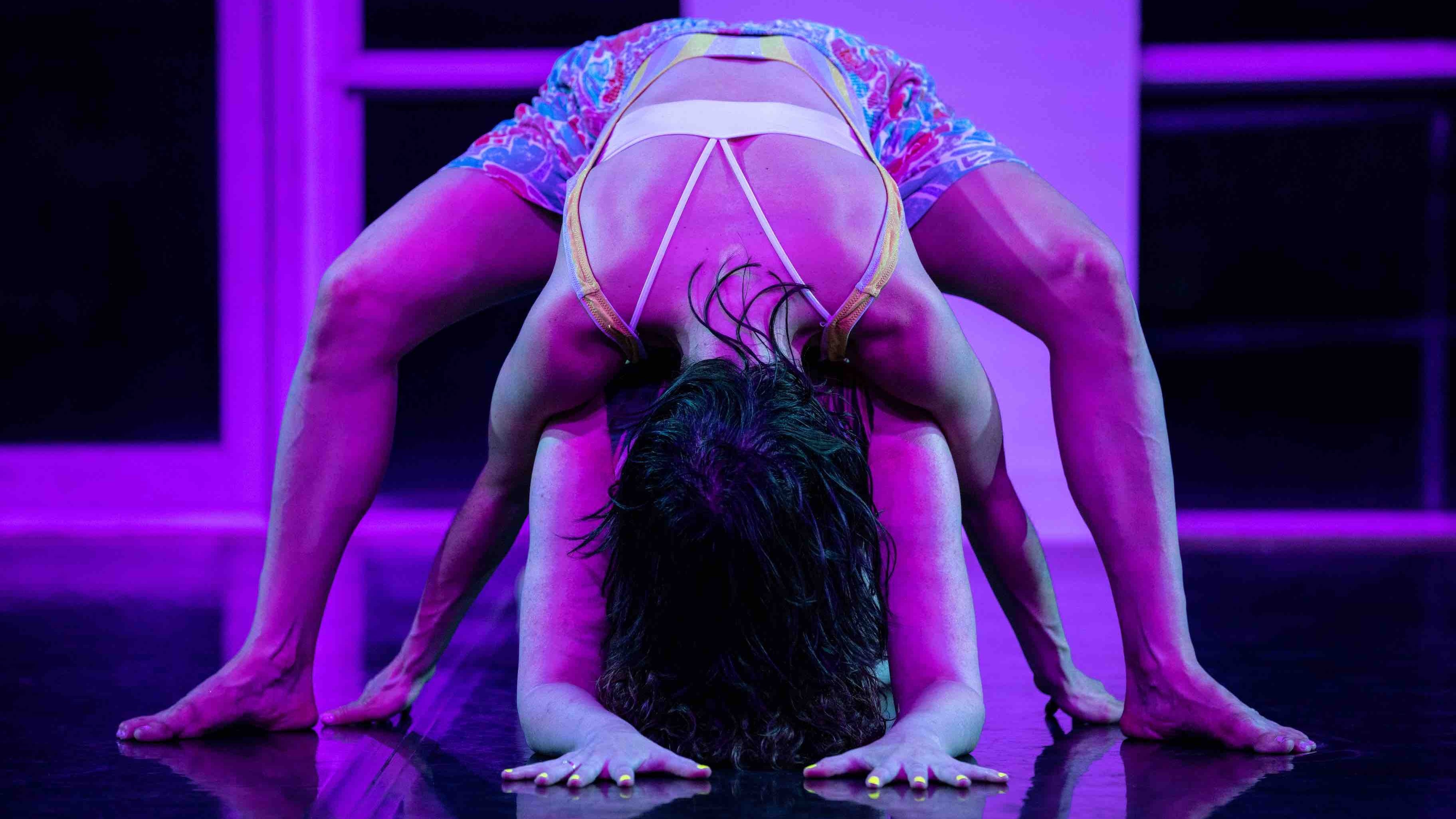 Two dancers leaning down with their thighs apart, one on top of the other