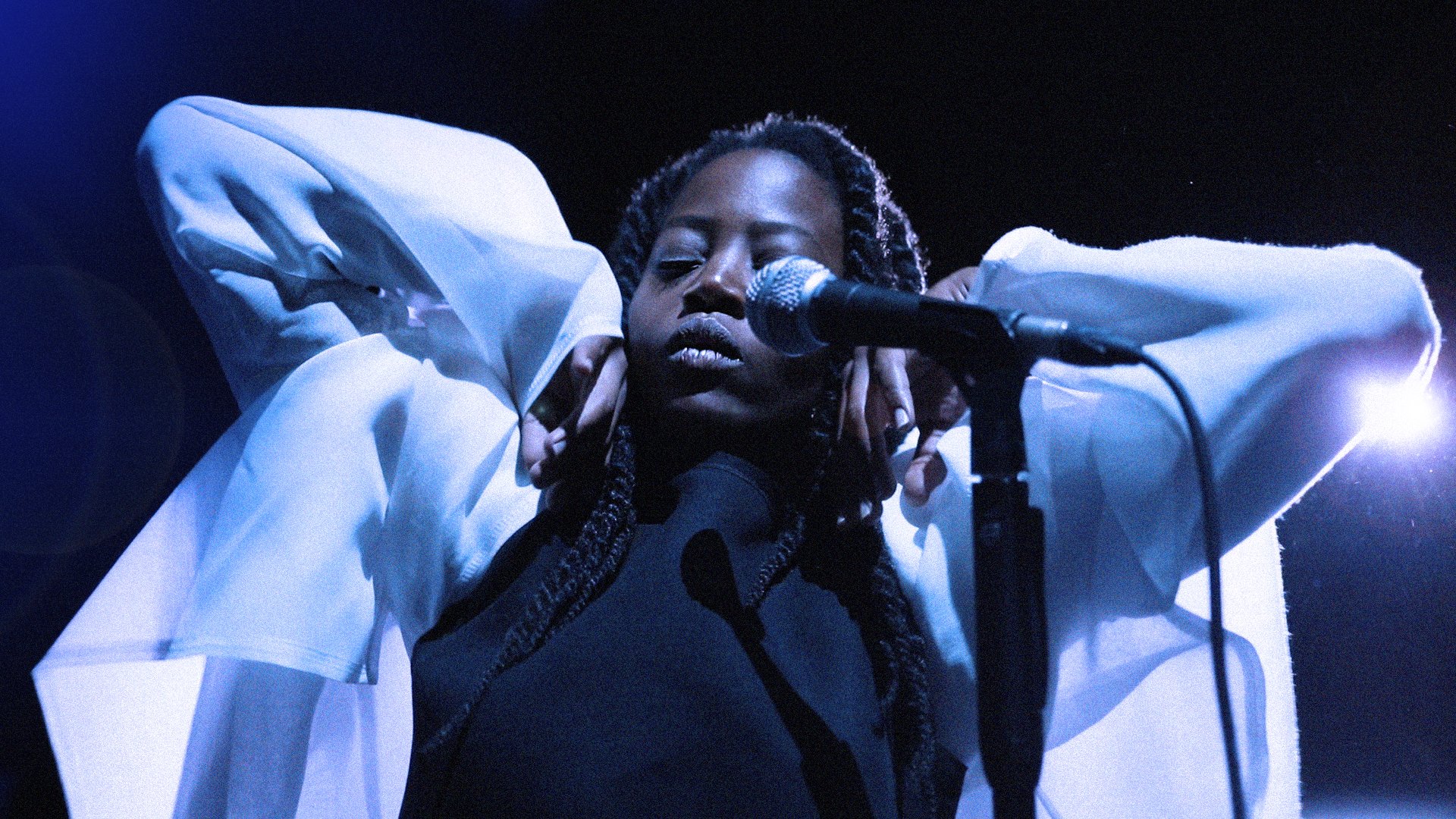 Woman behind a microphone, eyes closed, wearing a white jacket