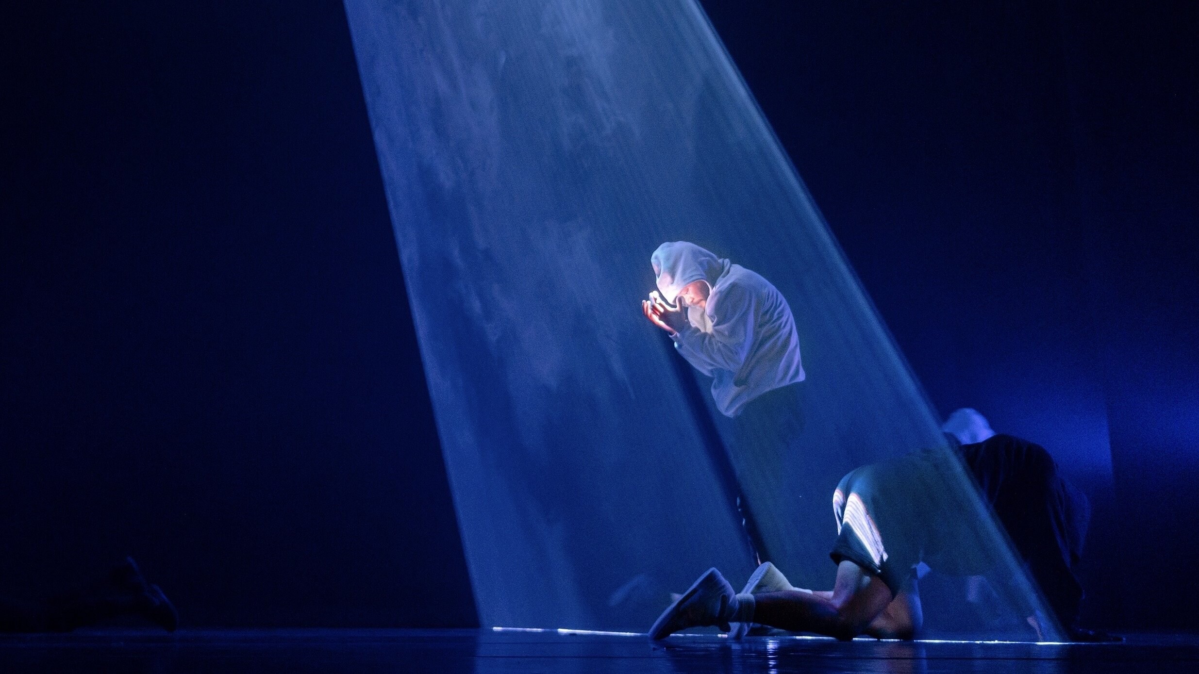 man in a hoodie, under a blue light, his head in his hands.