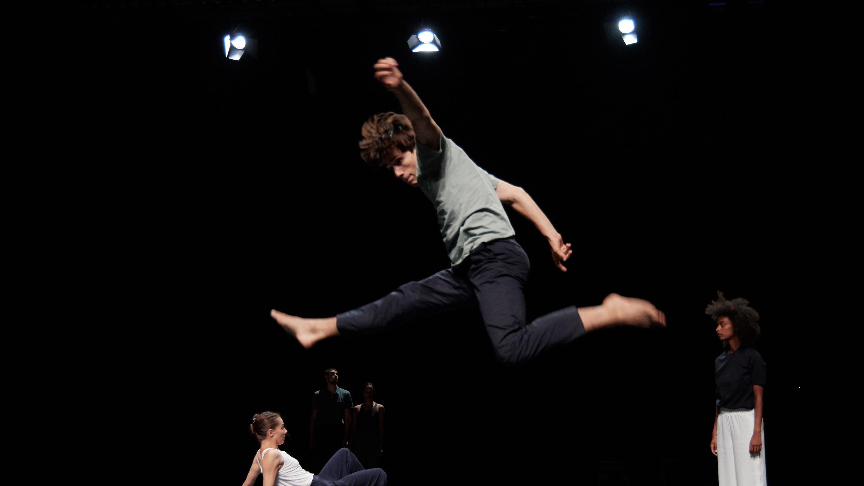 在空中跳躍的舞者。舞台上，另外有兩位舞者在後方。