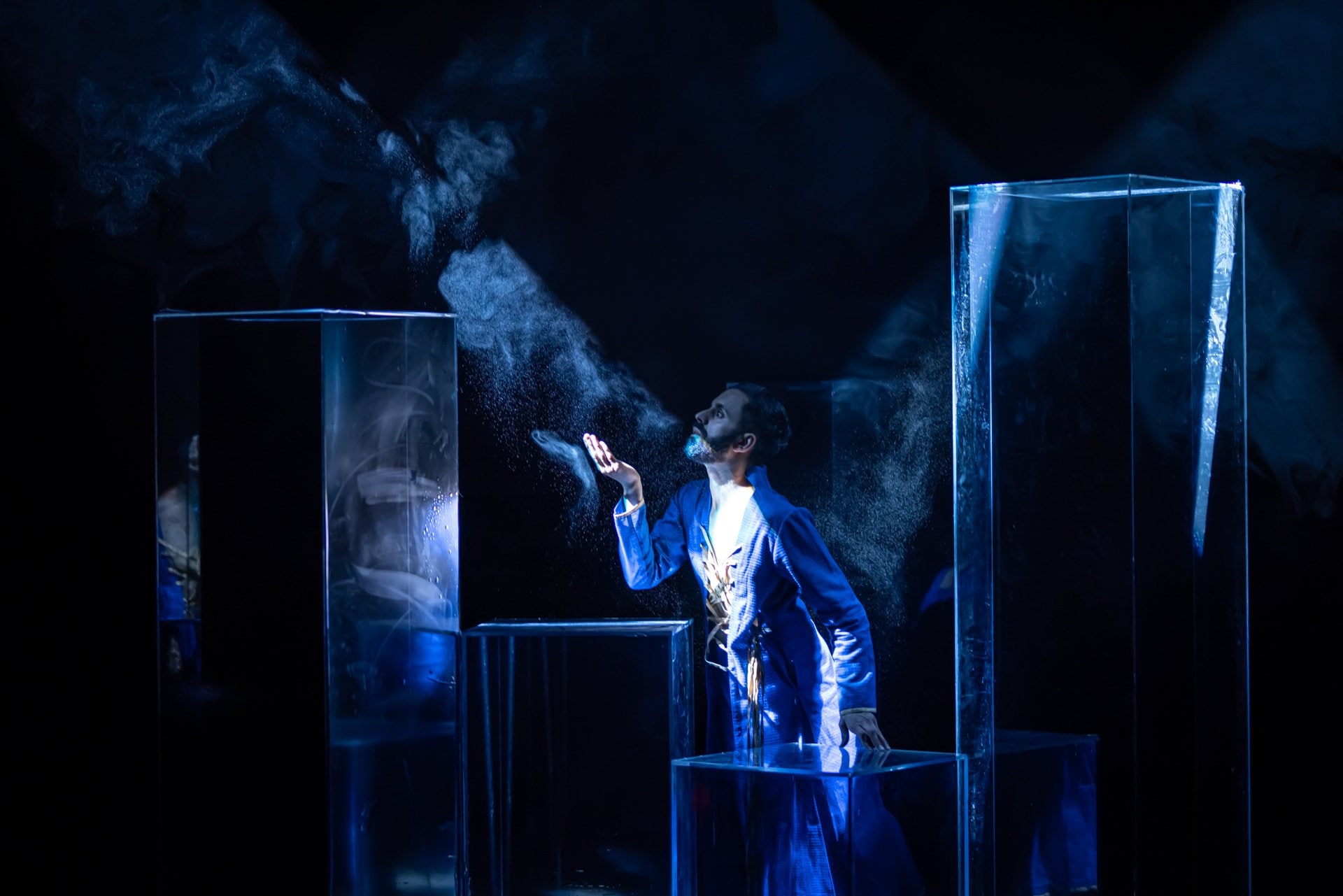 Aakash Odedra face à un rayon de lumière sur scène, dans une tunique bleue.