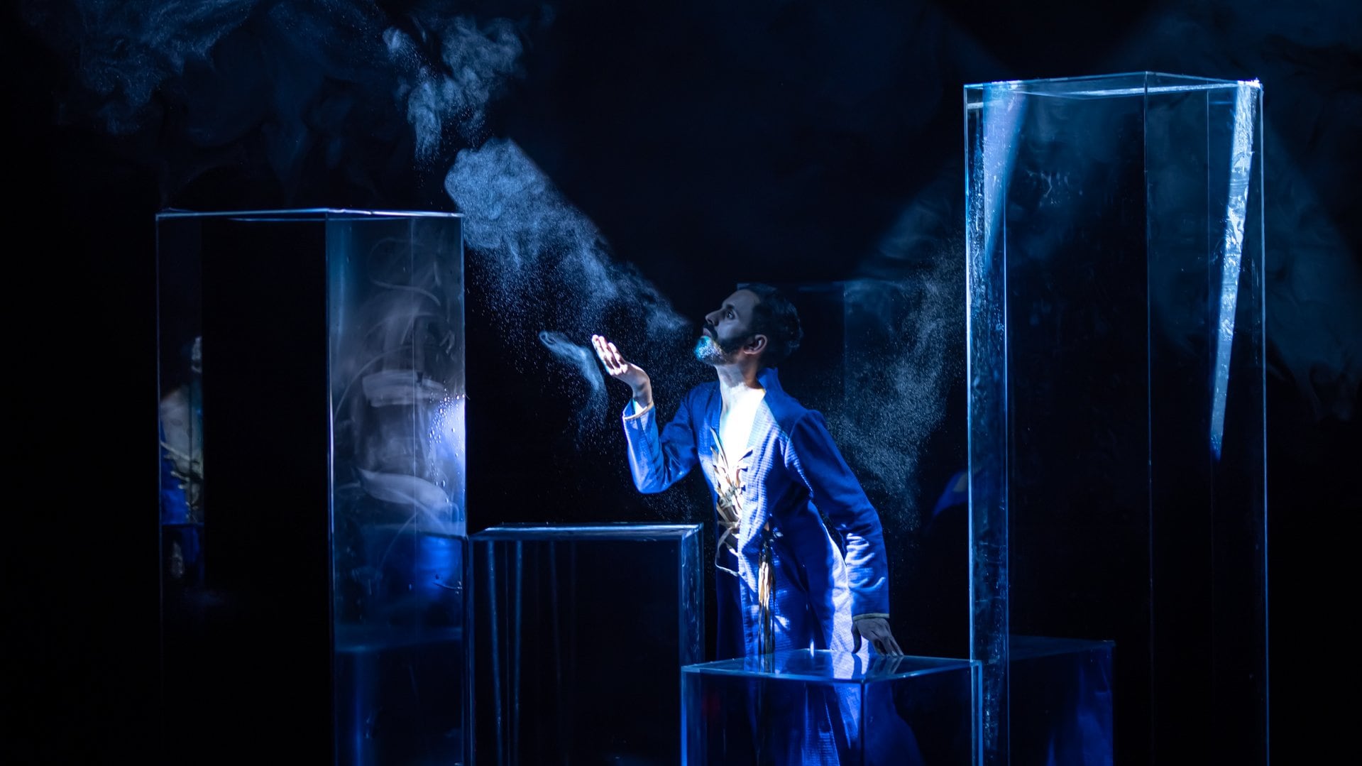 Aakash Odedra facing a ray of light on stage, in a blue tunic. 