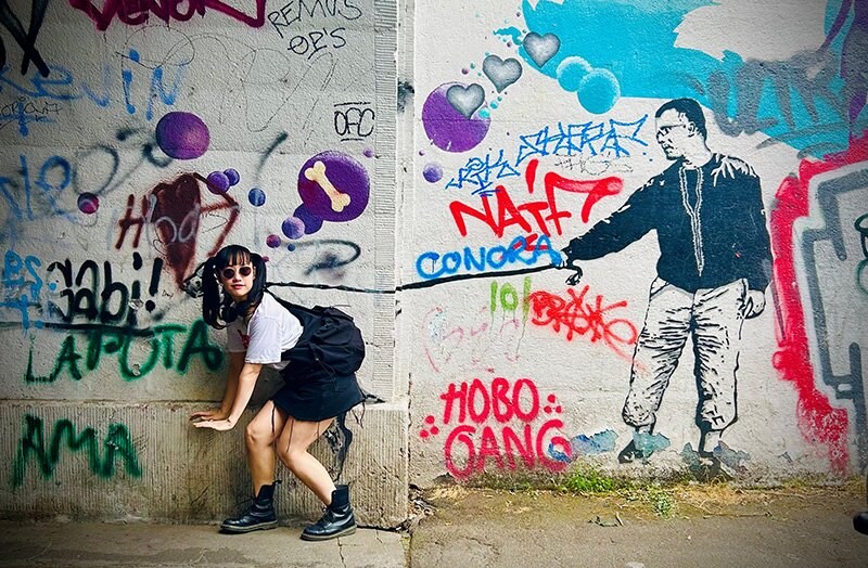 Fille en jupe noire devant un mur couvert de graffitis 