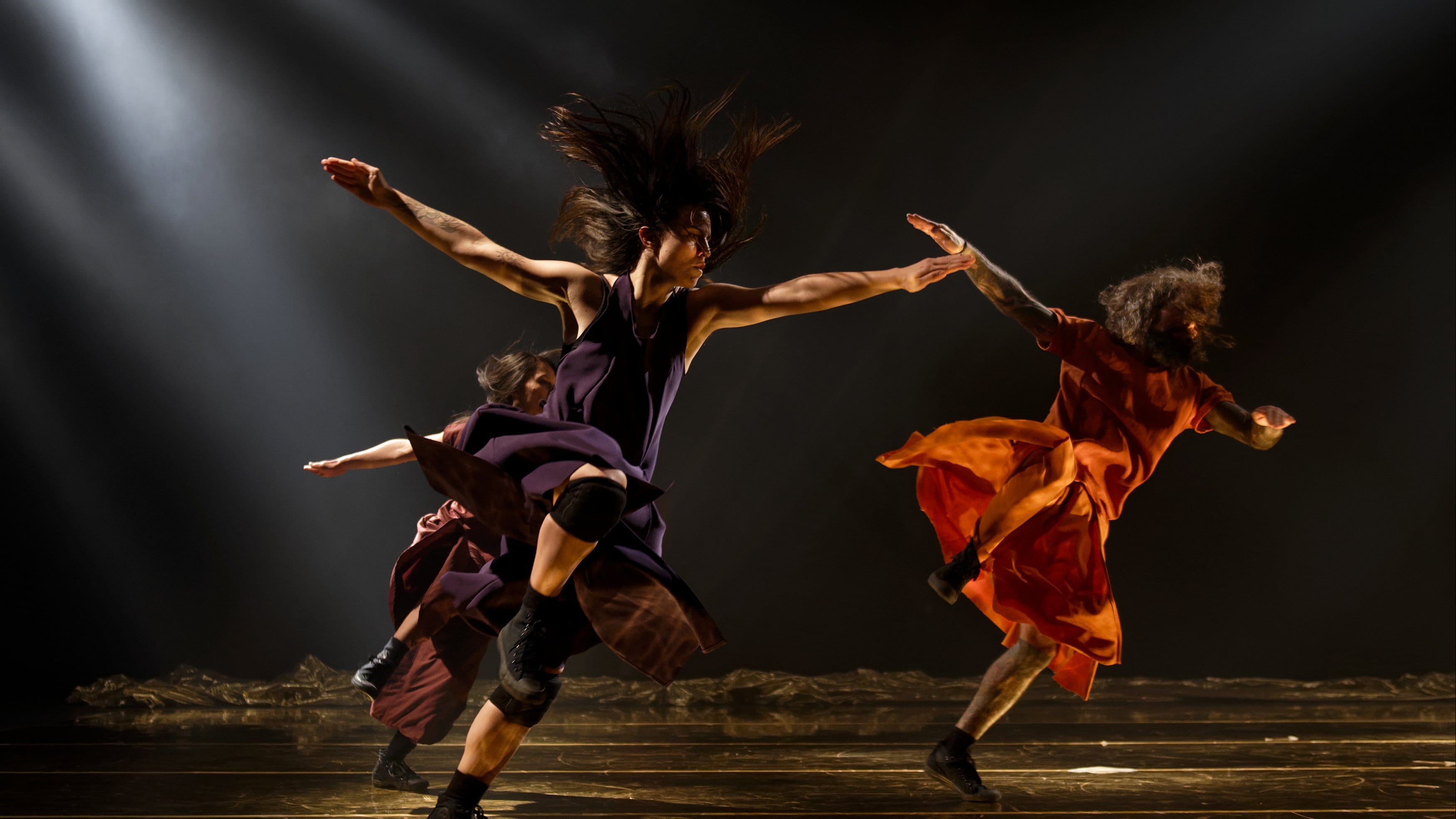 Trois danseurs sautant sur scène les bras ouverts