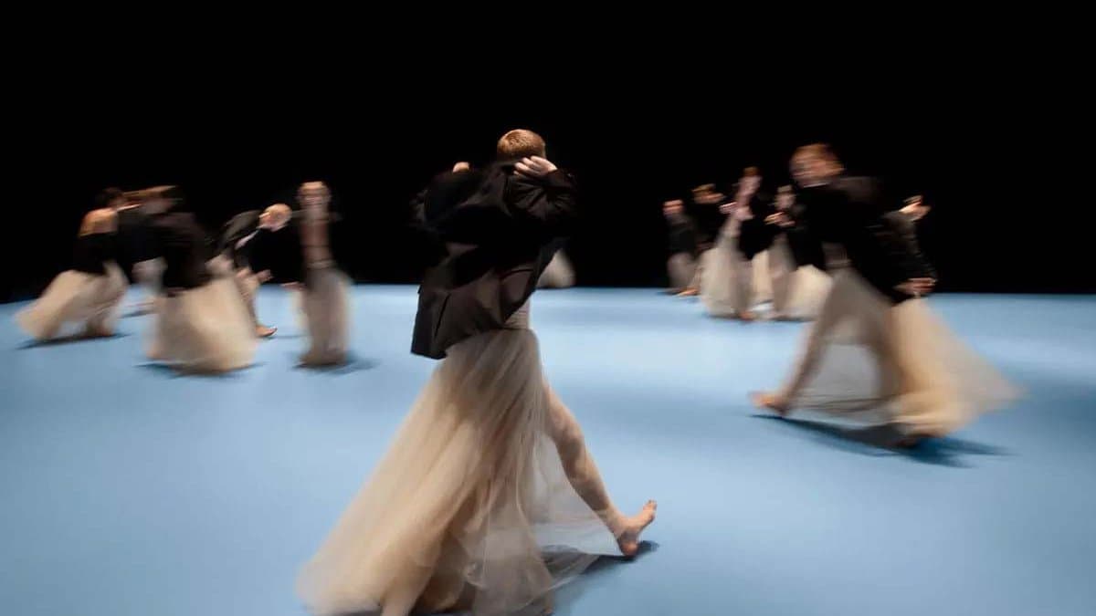 Dancers wearing pale pink long tutus and black jackets are walking