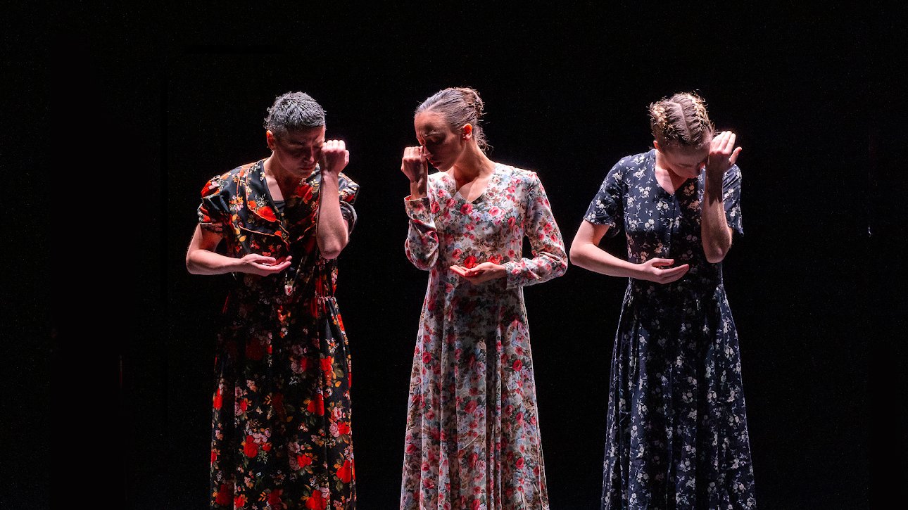 Three women in dresses, standing with hands on their faces