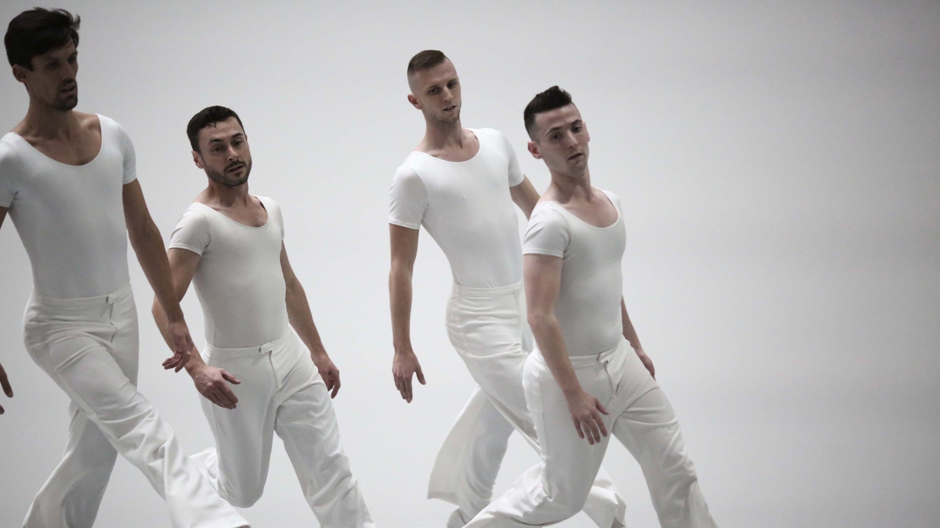 Four dancers dressed in white run on a white stage.