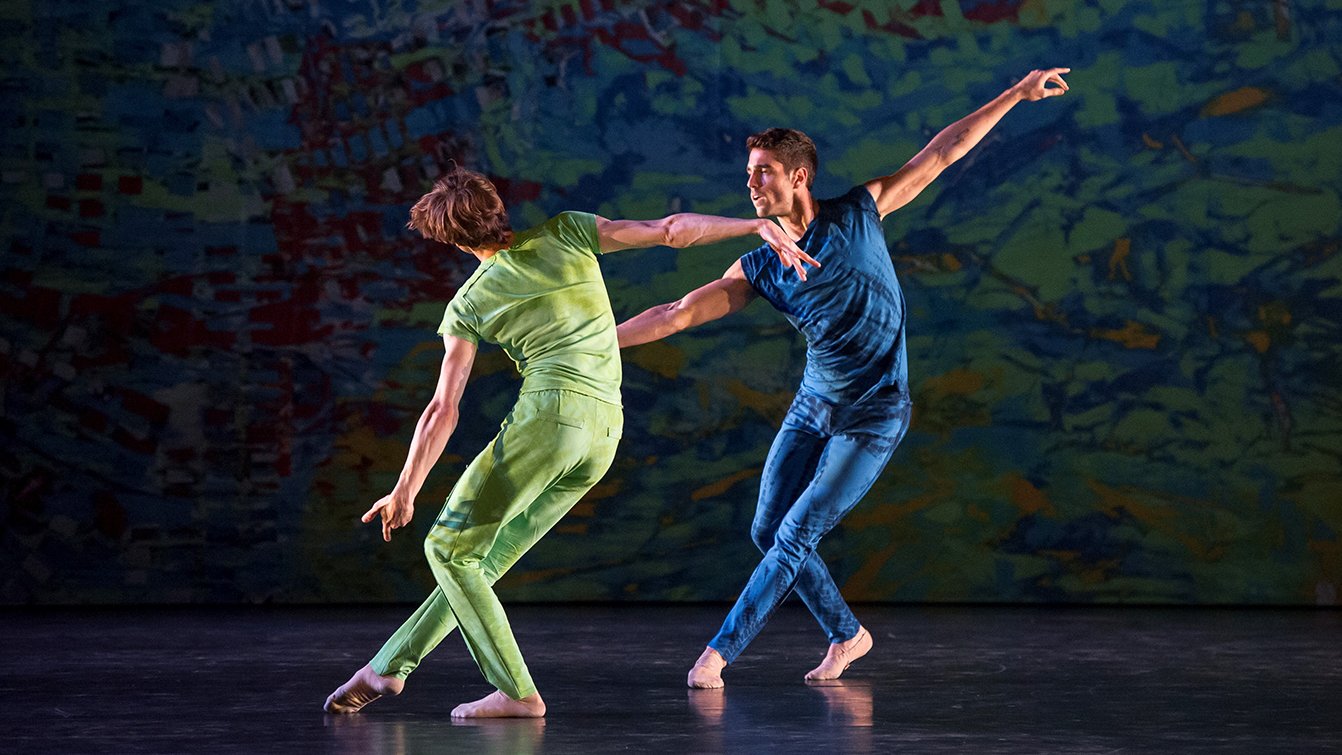 Two men, one in a green suit, the other in a blue suit on stage.