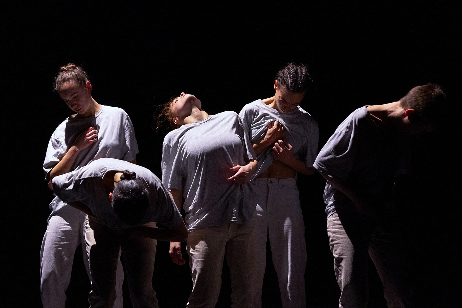 Five women dressed in a grey t-shirt and white pants in the dark 
