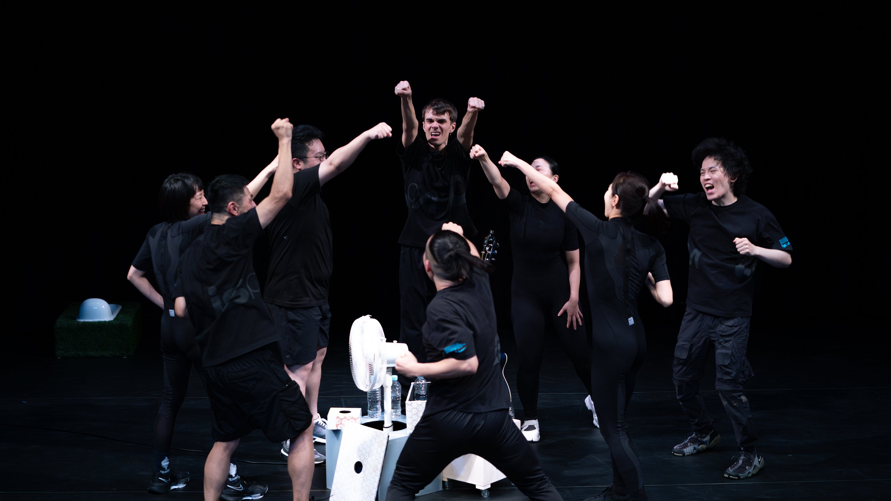 group of dancers in black clothing on stage, with several raising their fists
