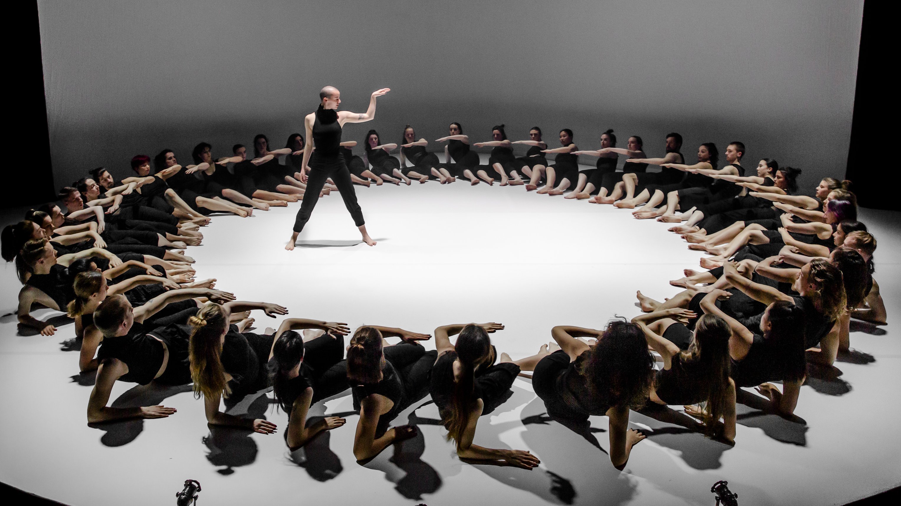 a dancer surrounded by a big cercle made by dancers lying on the stage