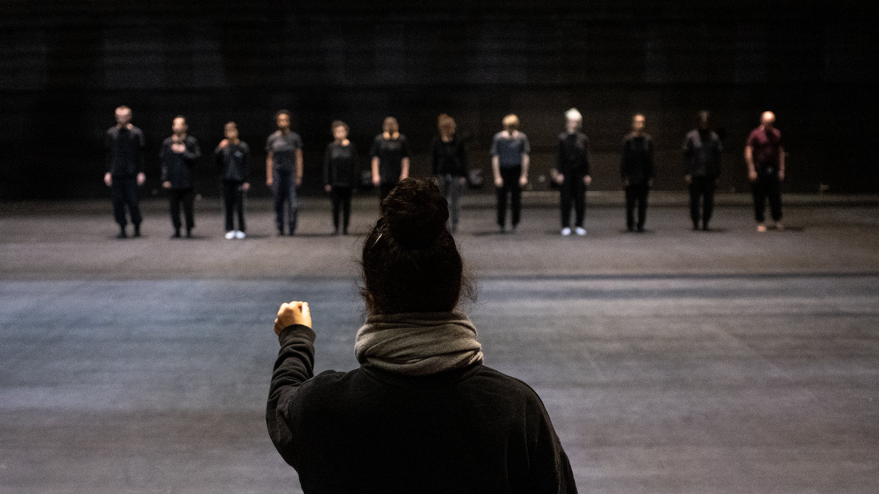 Nacera Belaza de dos et face à elle 12 danseurs en ligne vêtus de noir