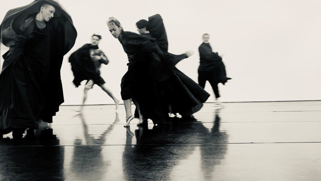 plusieurs danseurs sur scène vêtus de costumes noirs fluides