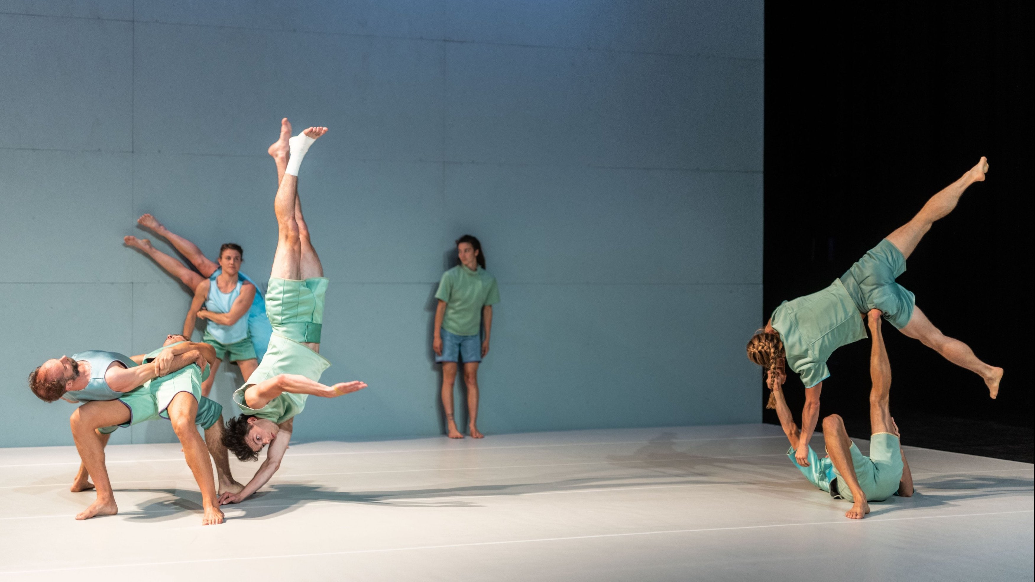danseurs en tenues claires effectuant des portés et des figures acrobatiques sur scène