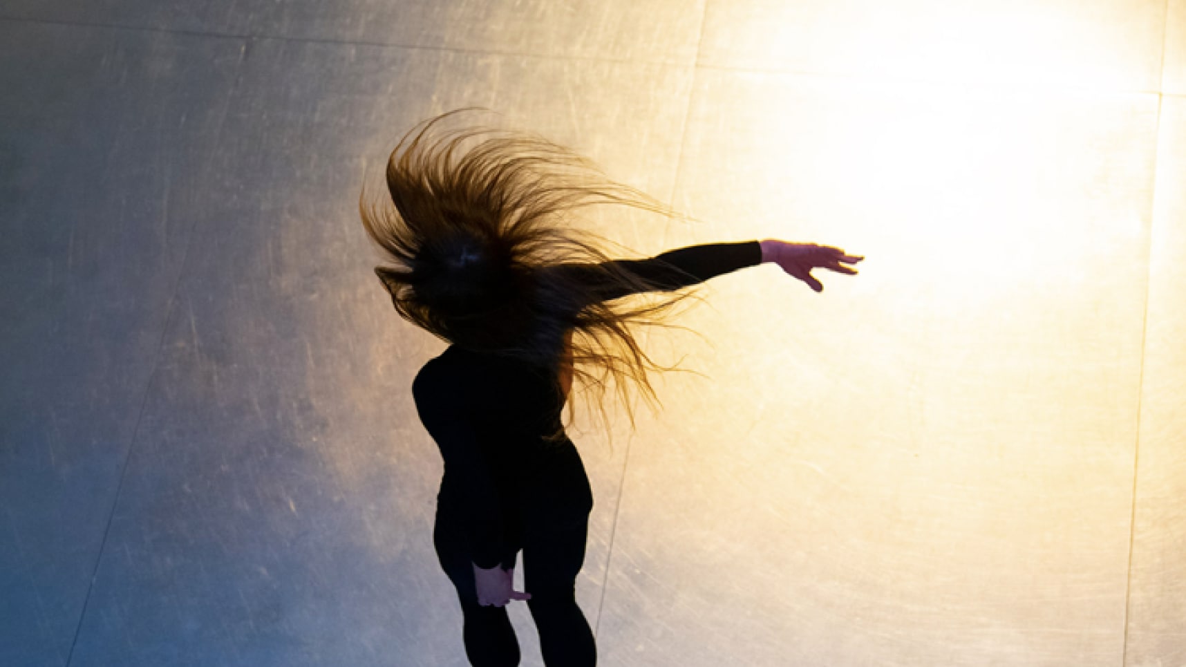 Dancer in black, hair flying, arm extended, on gradient blue background