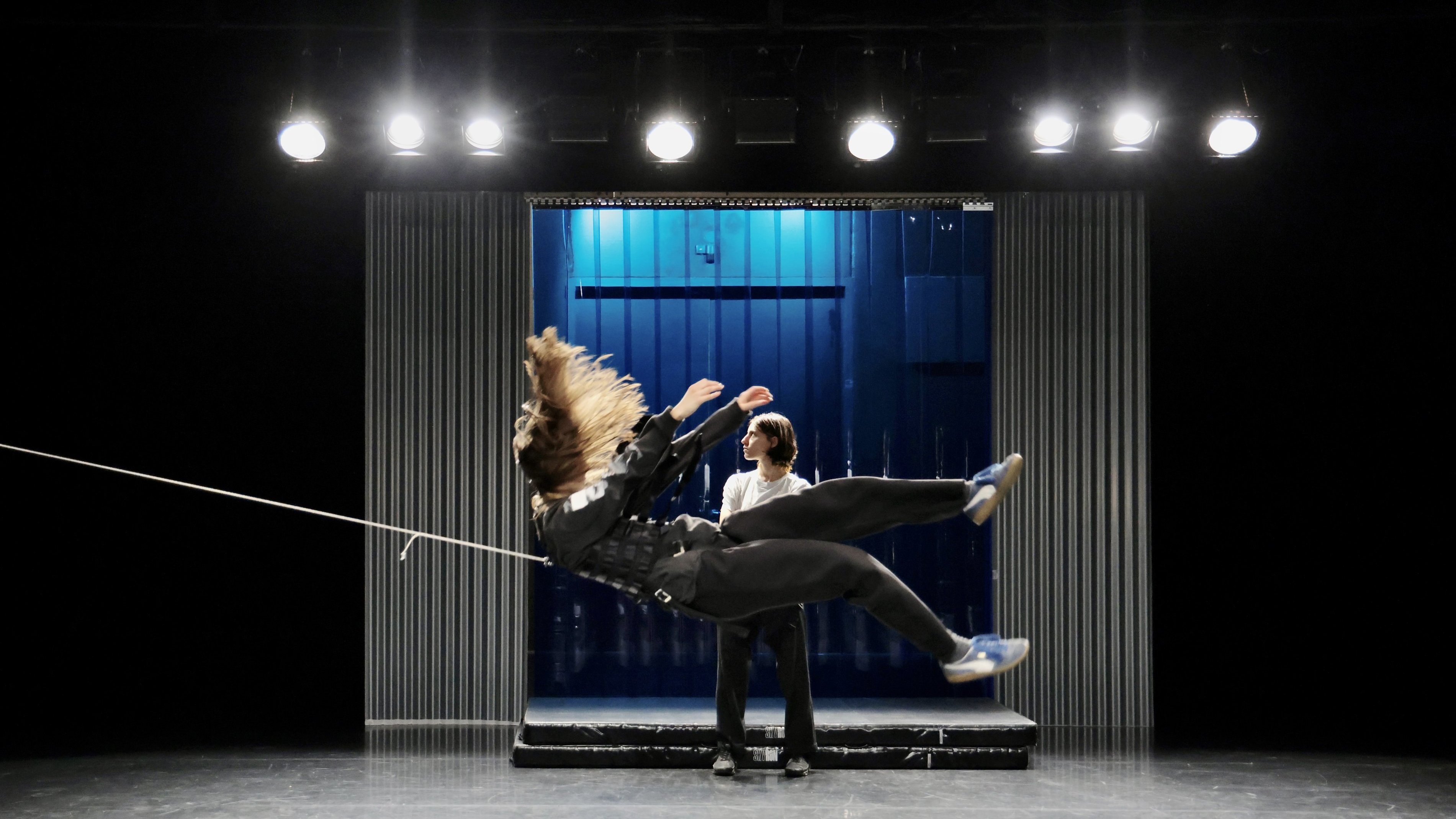 A dancer being pulled backward by a rope, with another person standing behind her