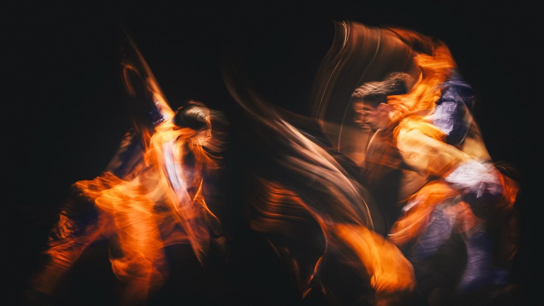Two blurred figures of dancers with orange light effects