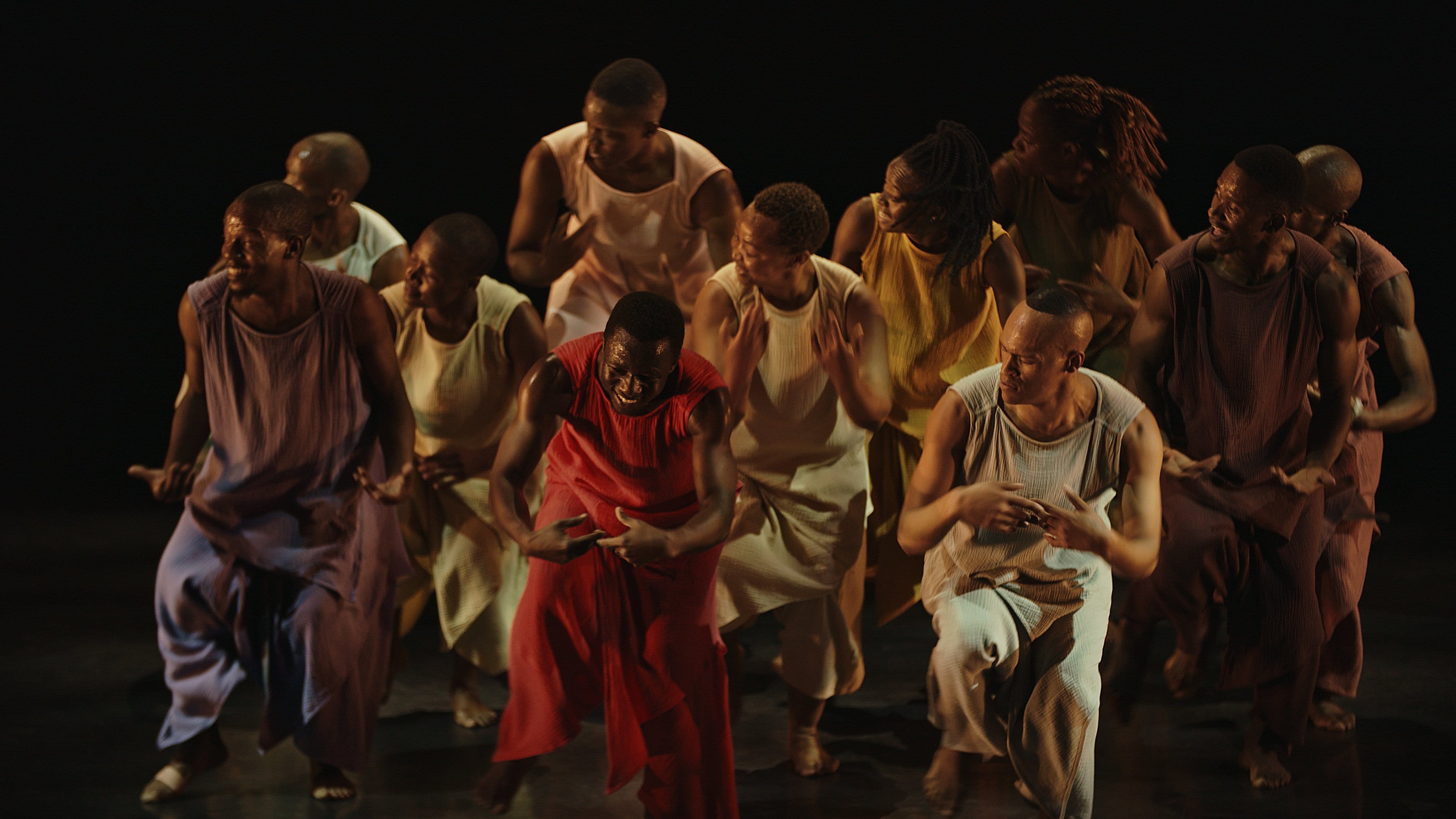 African dancers in traditional costumes of different solid colors on a black background