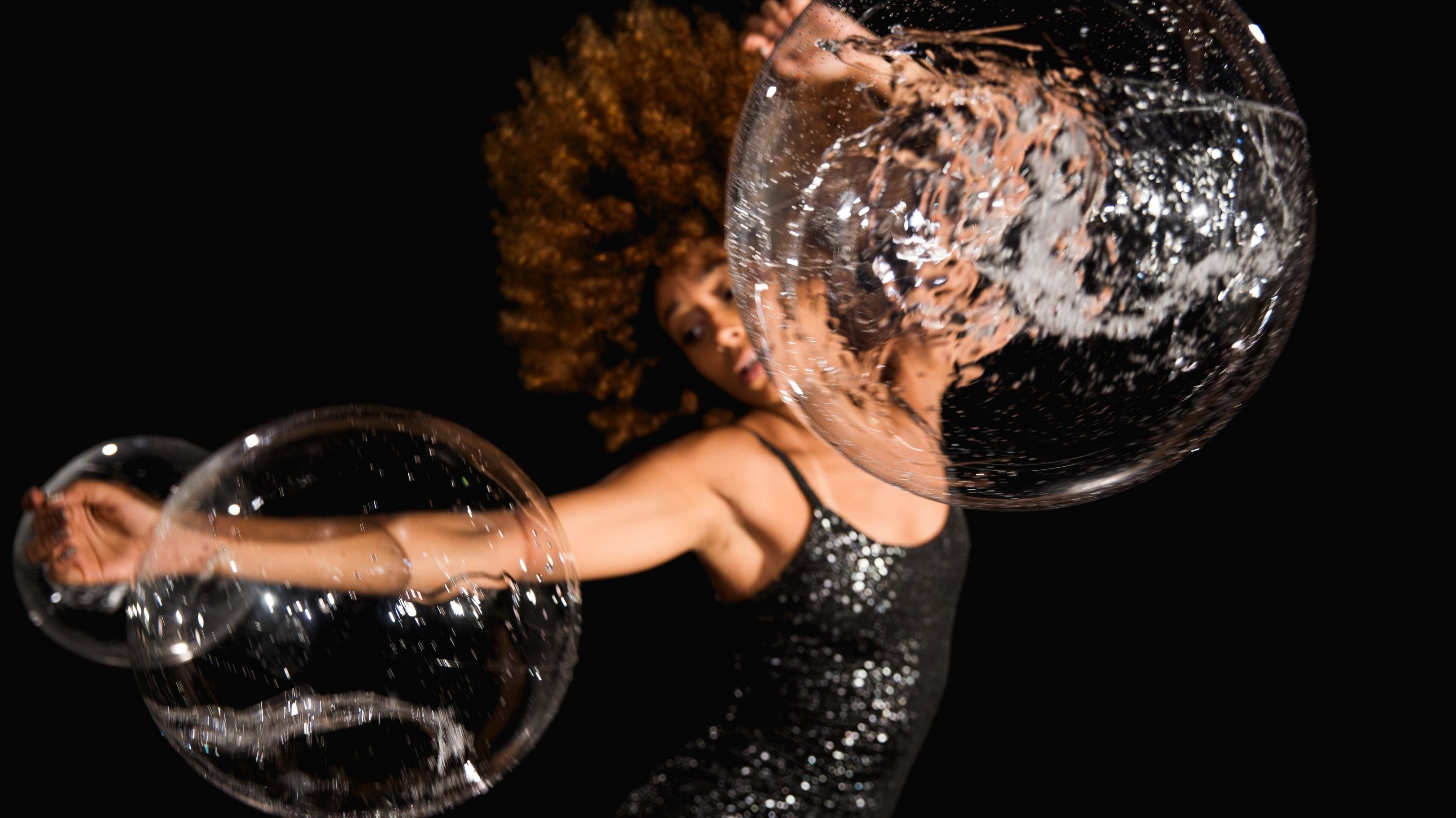 Une femme portant une robe pailletée danse avec des bulles. 