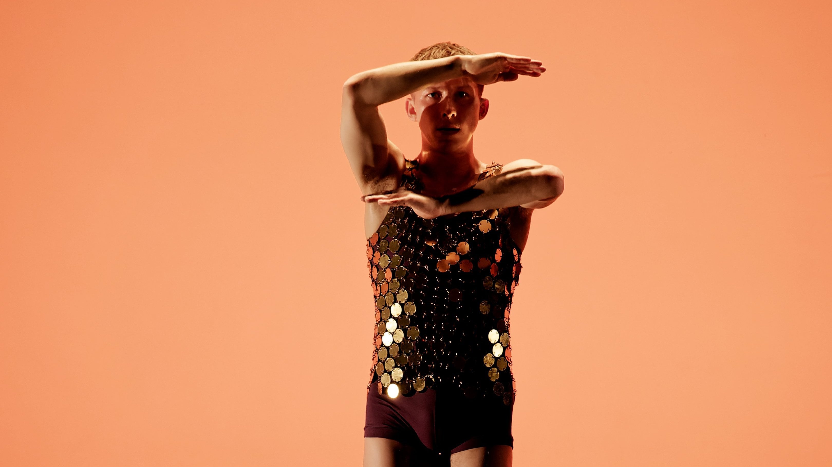 Danseur dont les bras sont pliés devant son visage, arrière plan orange.