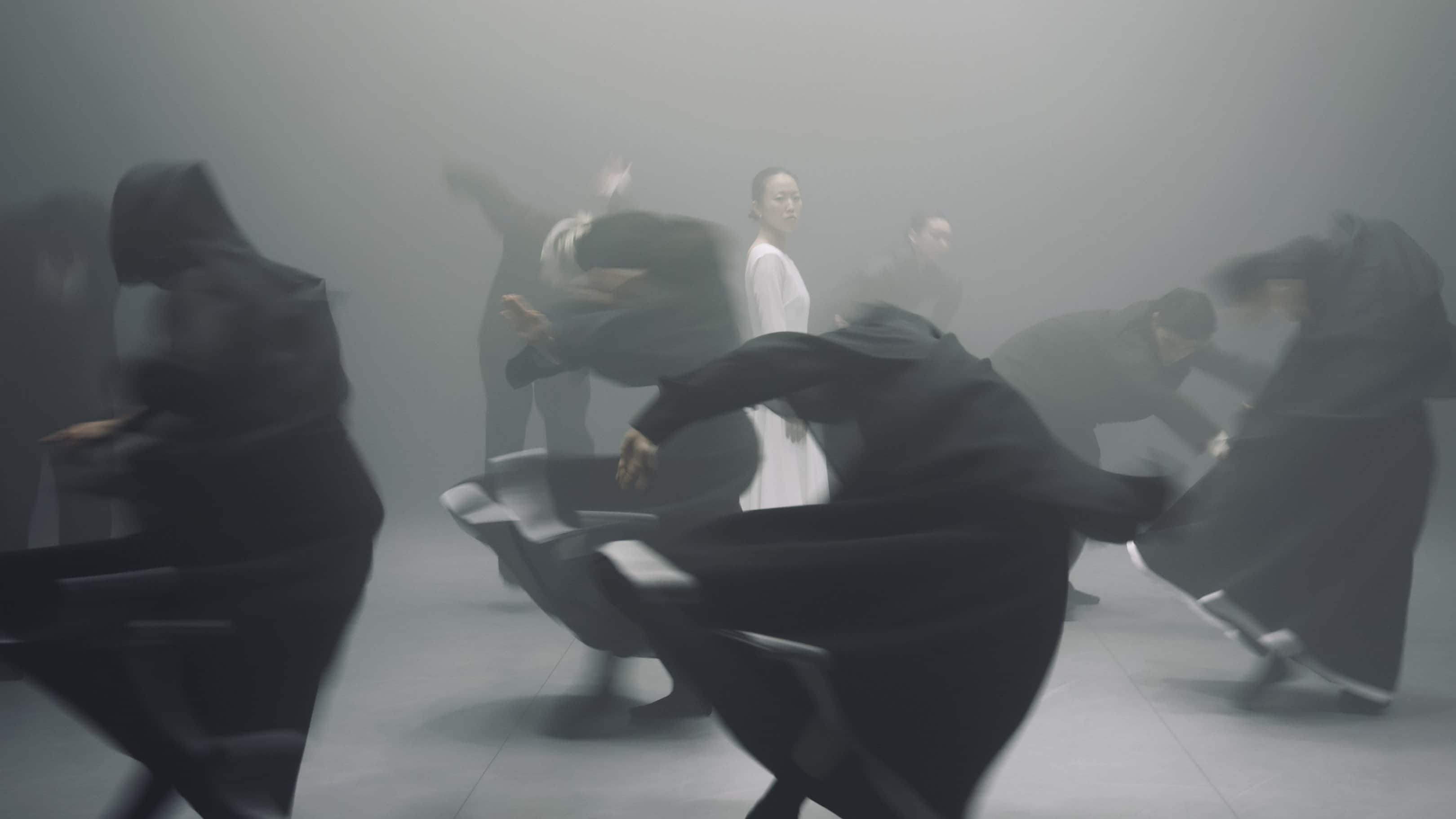 Danseurs en tenue noire  en mouvement tournant autour d'une danseuse dans une tenue blanche. 