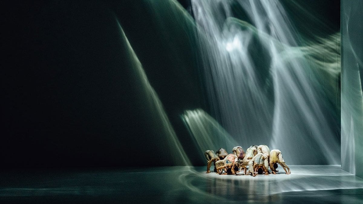 Un groupe de danseurs se rassemble et s'incline,  les mains effleurant le sol, baigné par une lumière  vaporeuse.