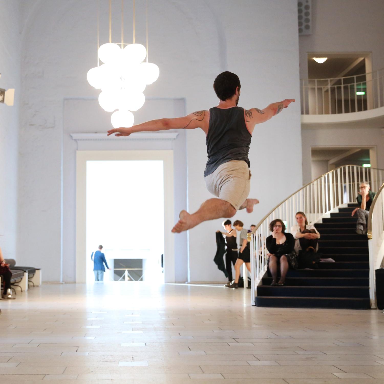 「在Boris Charmatz作品《20 danseurs pour le XXe siècle》的觀眾圍繞下，舞者跳起呈一字馬的背面圖」
