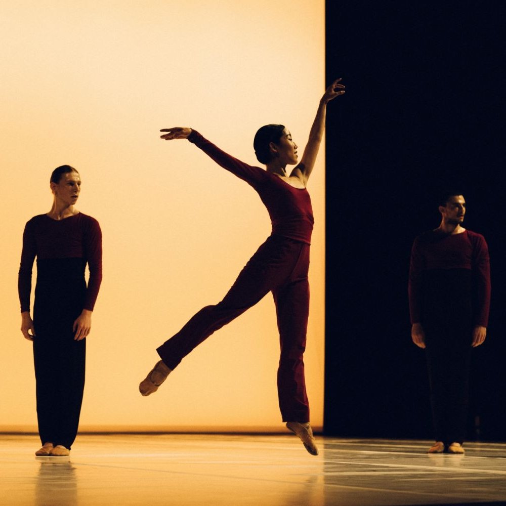 Leaping dancer in front of two static dancers on-stage