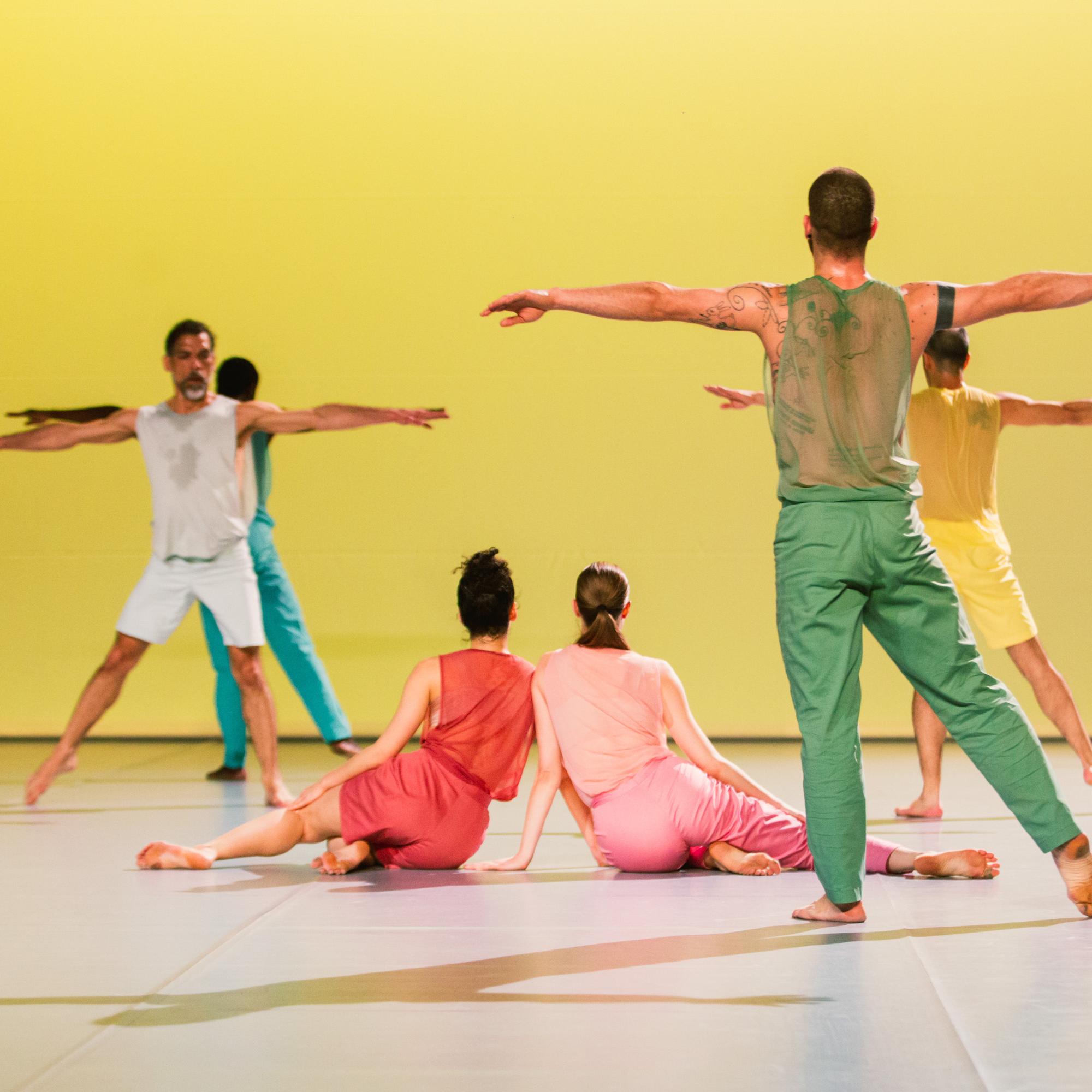 colorfully dressed up dancers on facing a yellow wall 