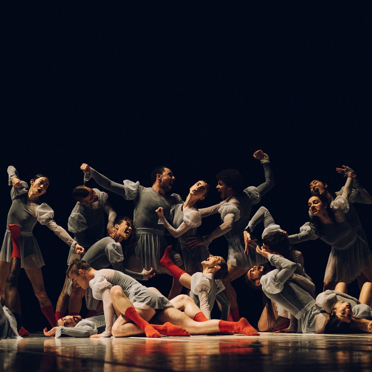 Group of dancers on-stage dressed in gray, with red socks