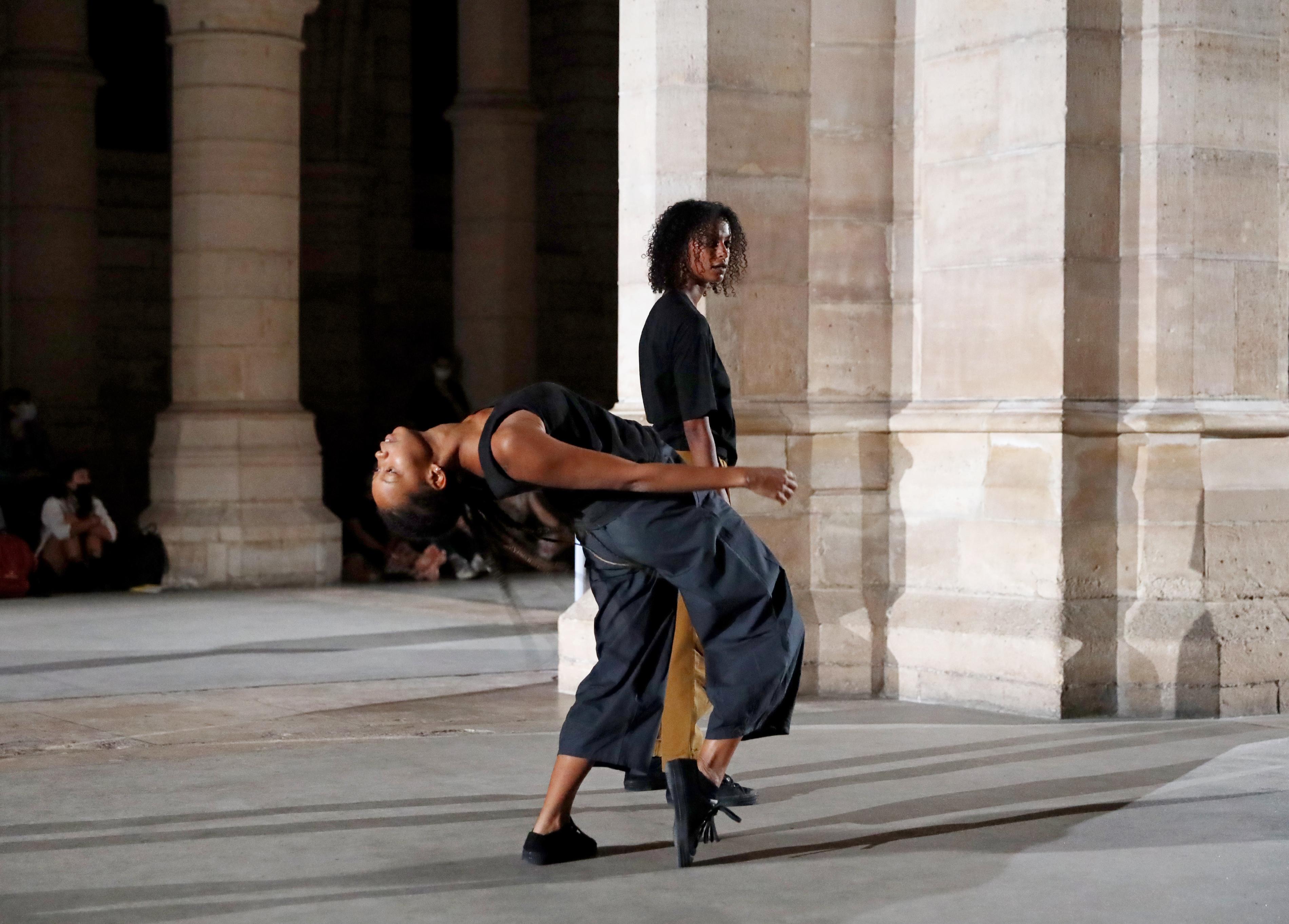 在一個充斥著柱子的空間內，一位舞者站在另一位舞者身後，身體向後仰