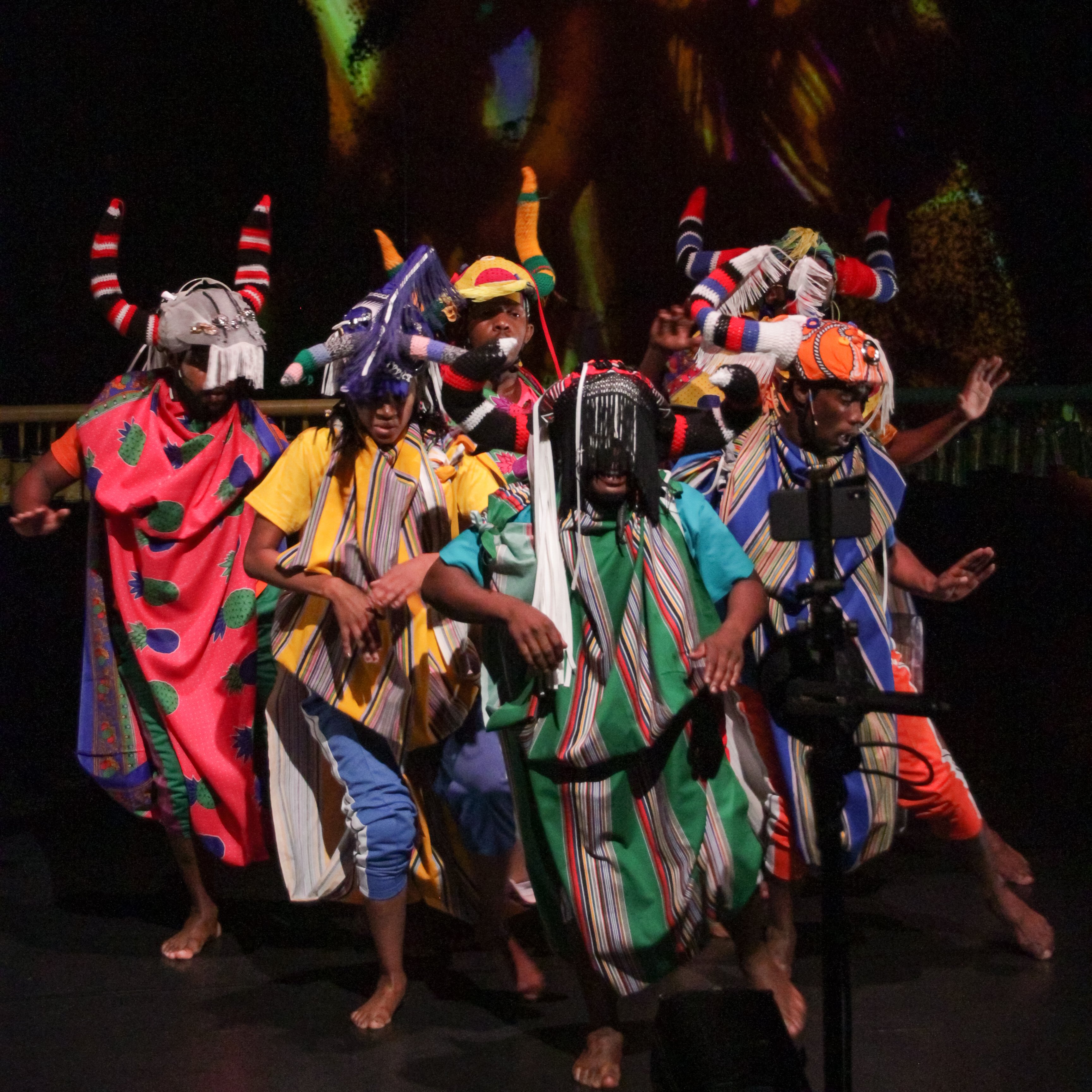 dancers dressed in colorful printed fabrics and headdresses on a dark stage