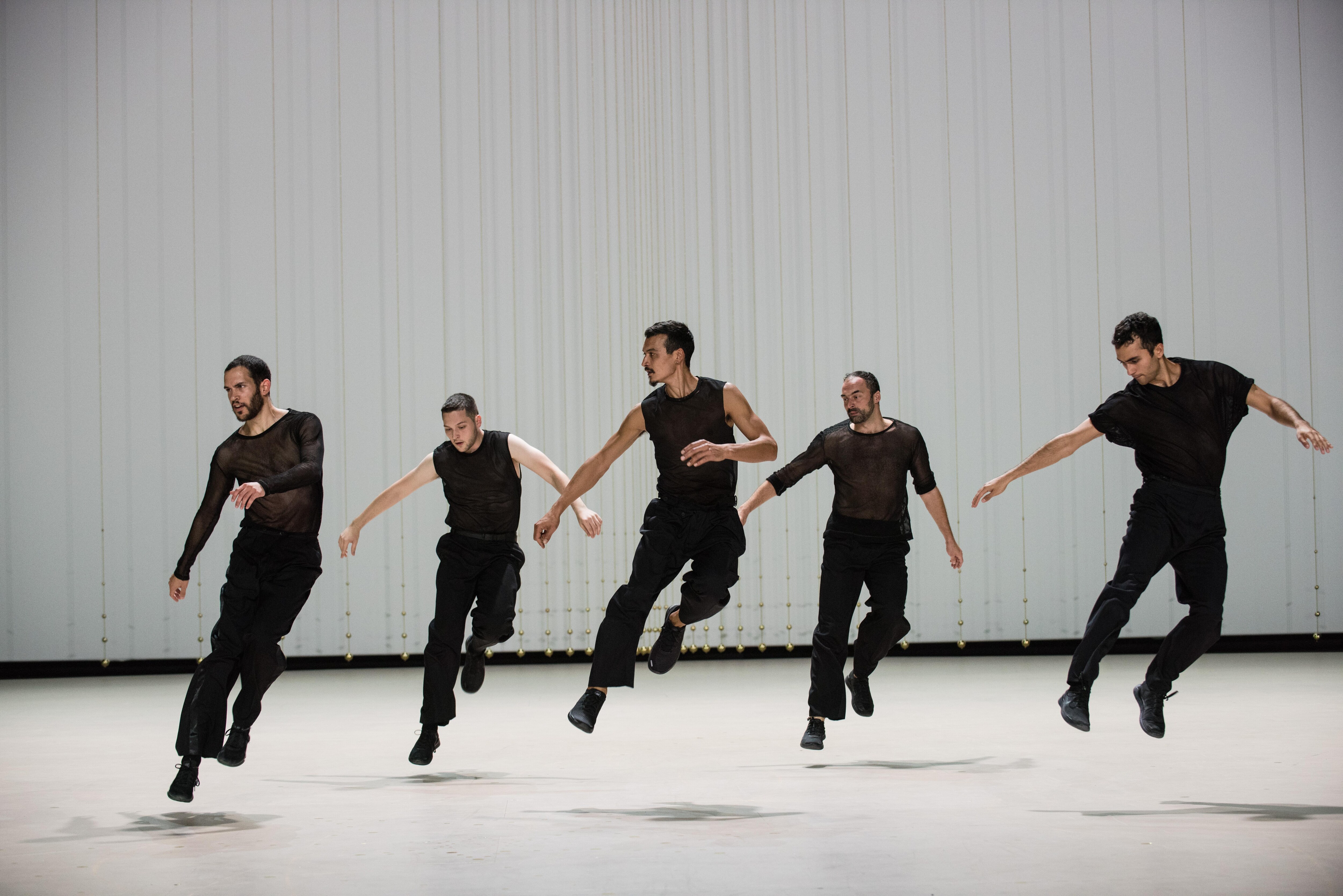 Five dancers wearing black, jumping