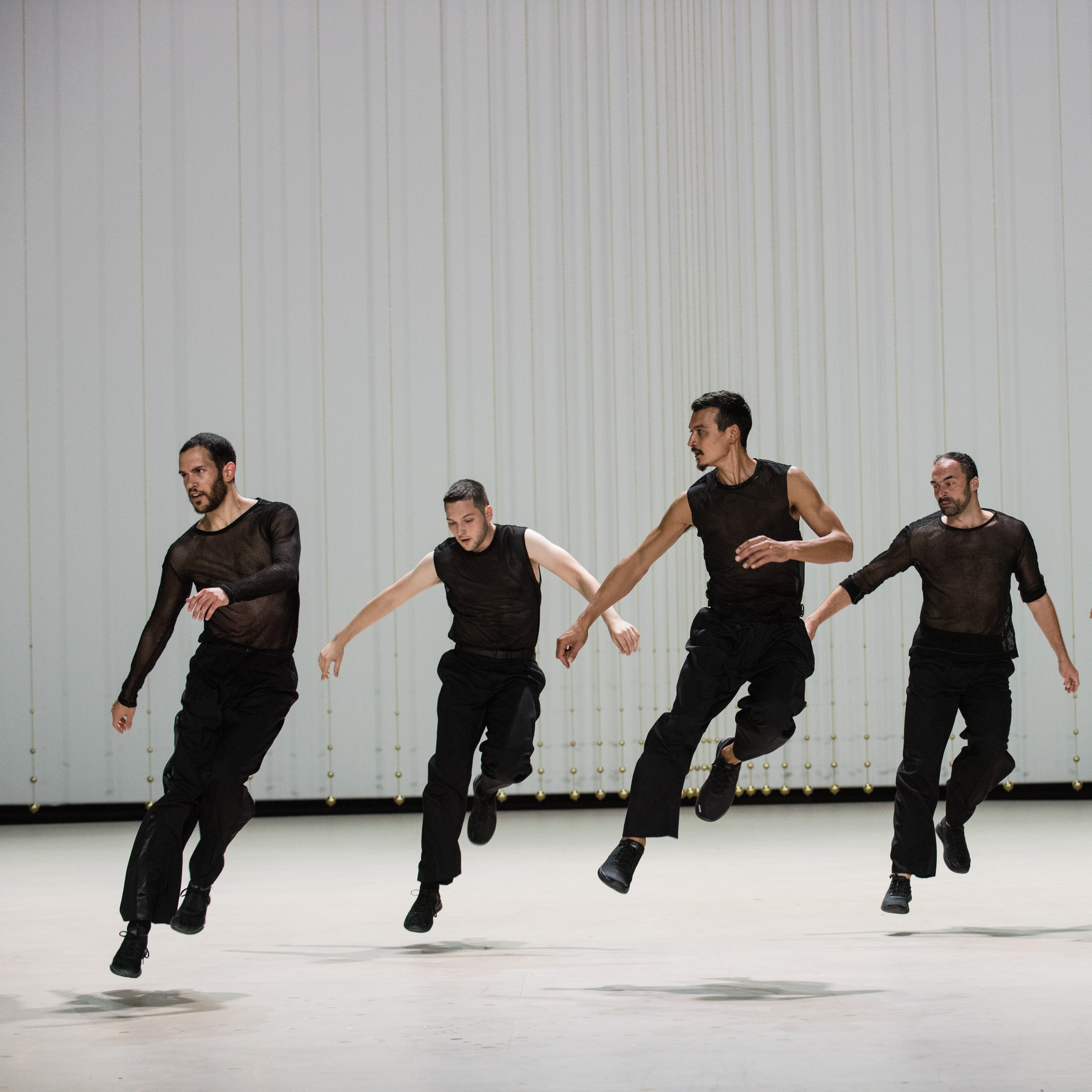 Five dancers wearing black, jumping