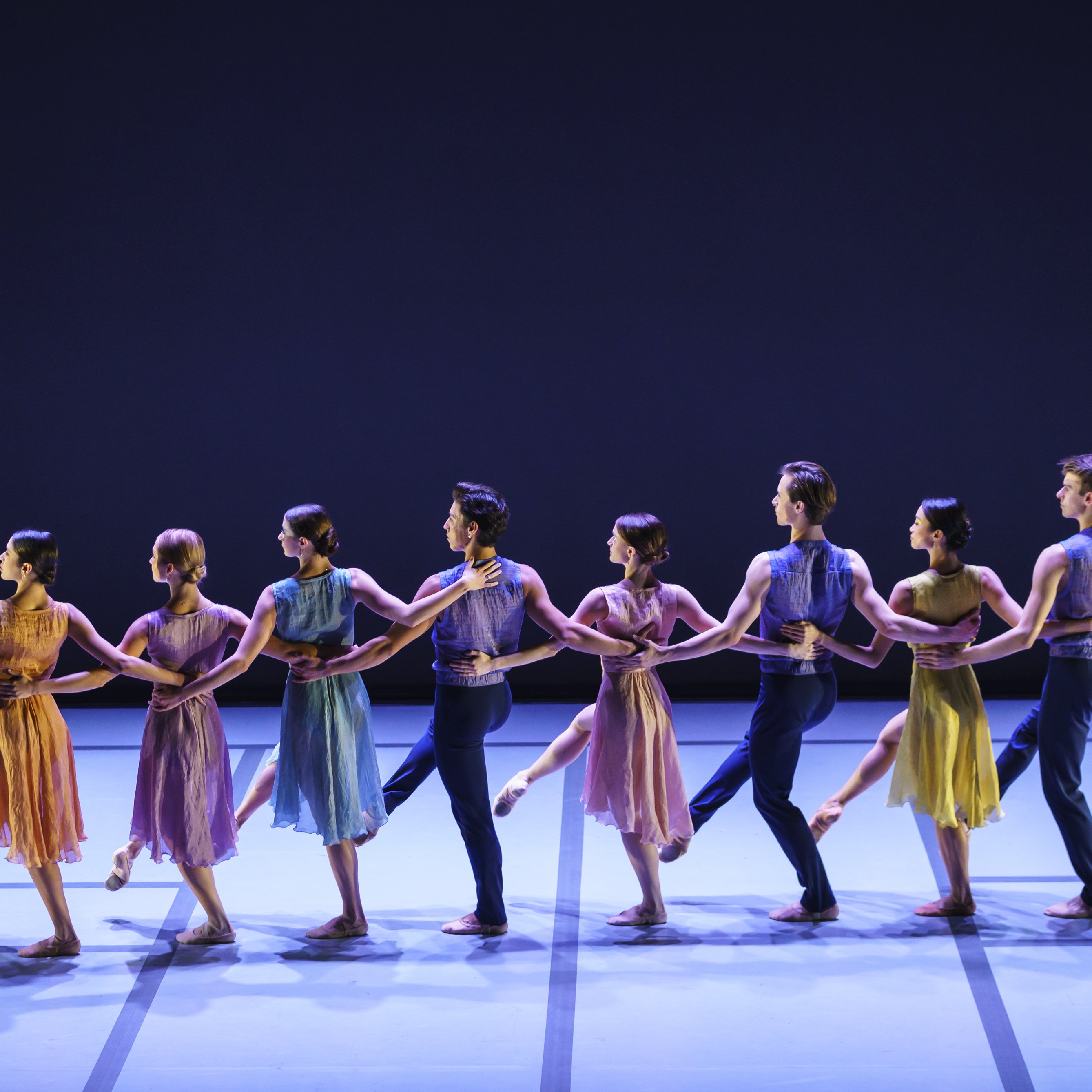 Dancers in line facing the back of the stage, holding each other by the waist