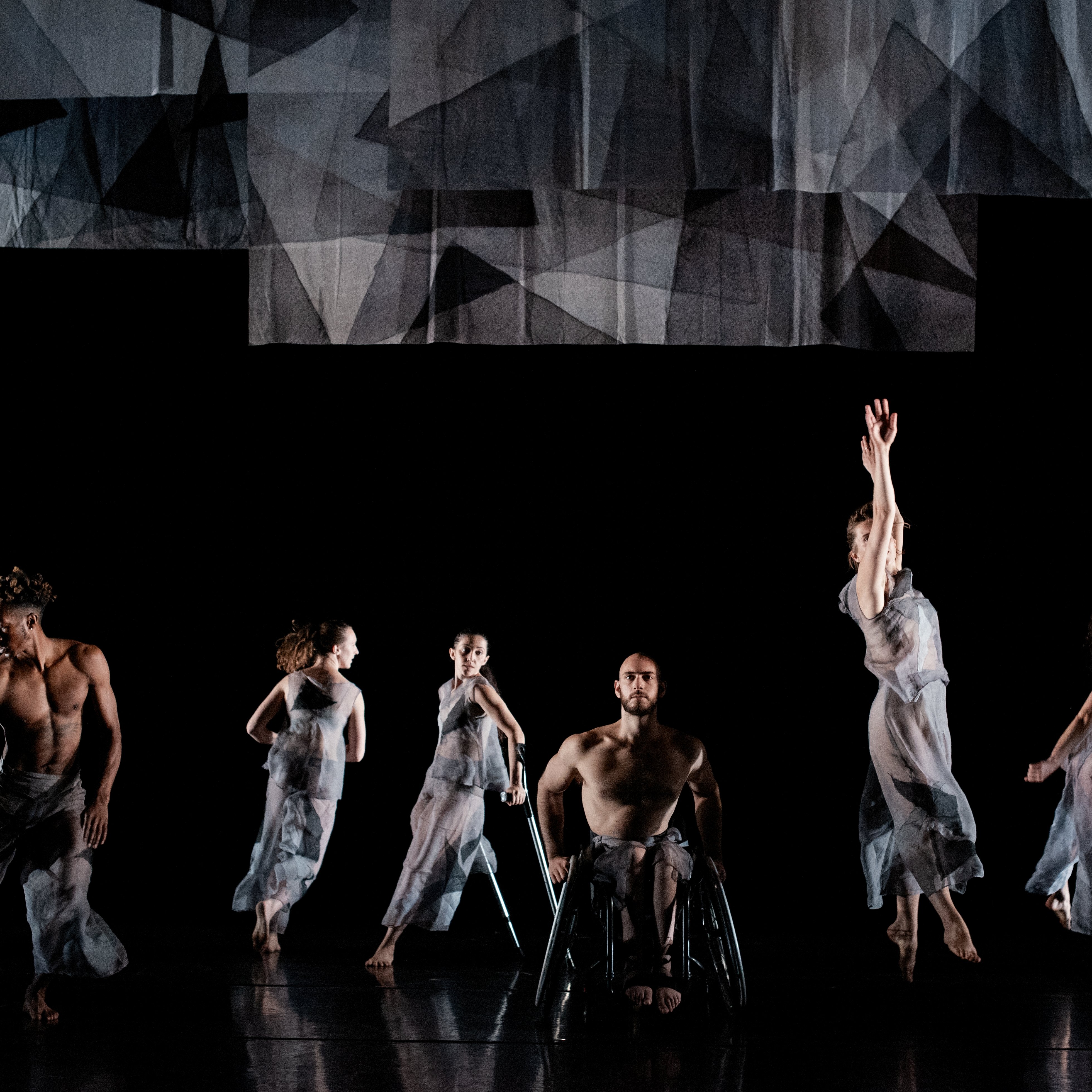 Six Dancers dressed in see-through grey clothes dancing on a black stage