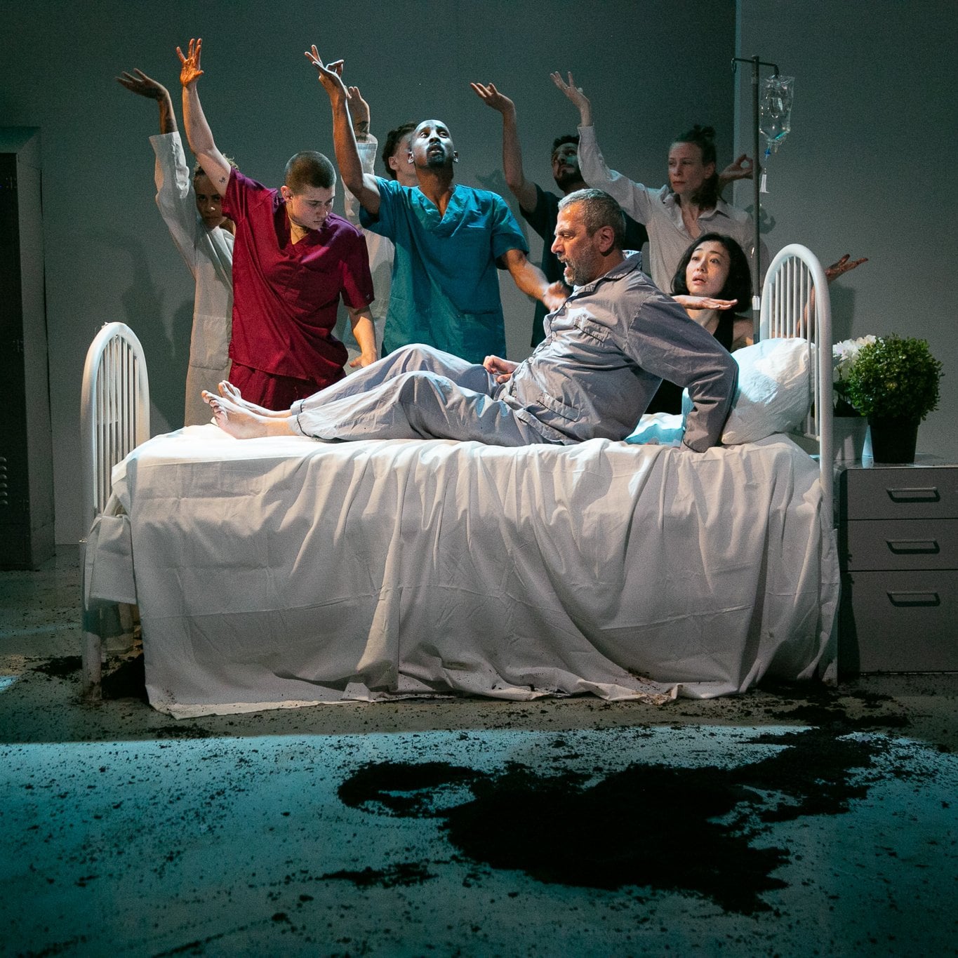 Dancers dressed as caregivers, surrounding a man on a hospital bed