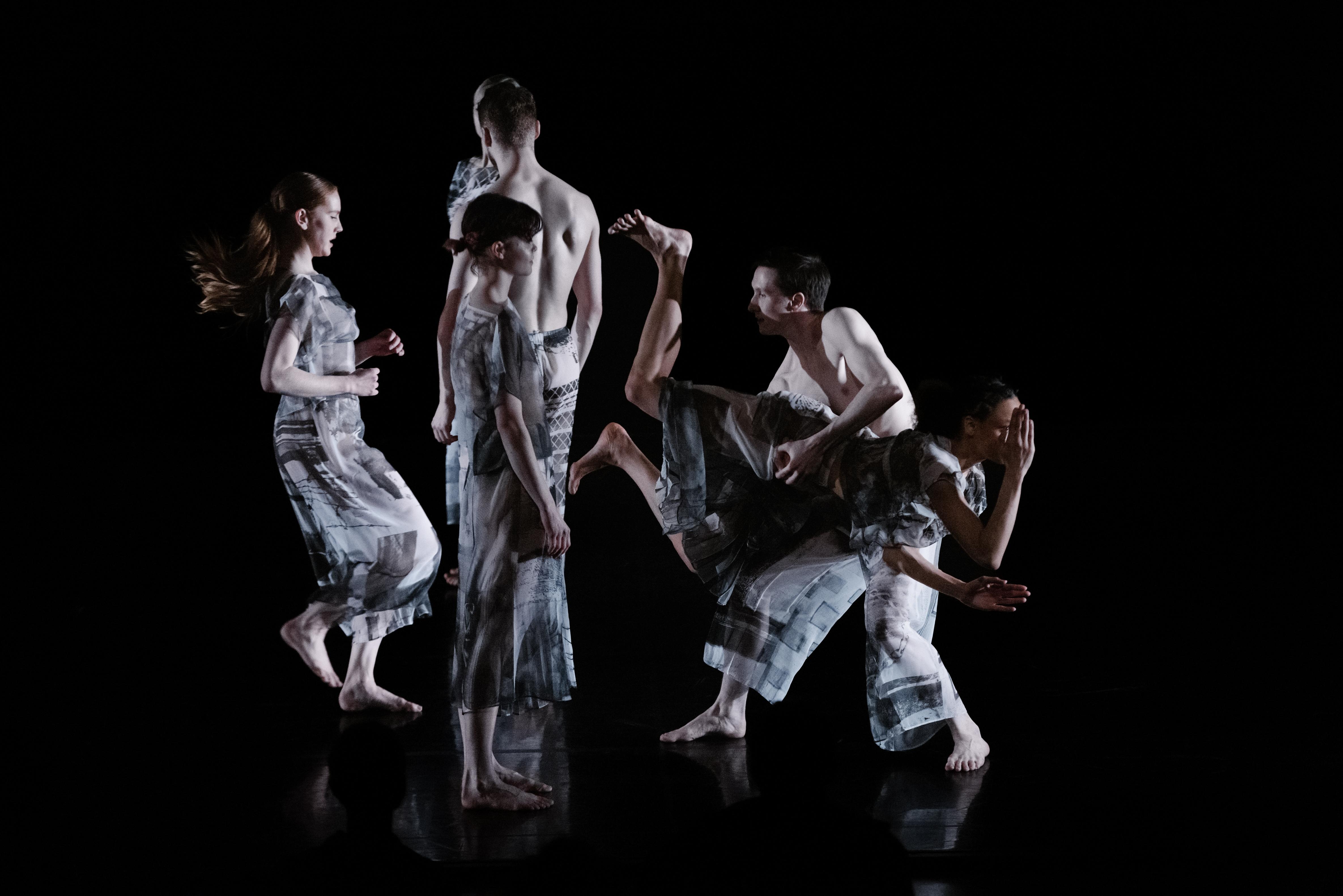 Cinq danseurs vêtus de gris sur une scène noire