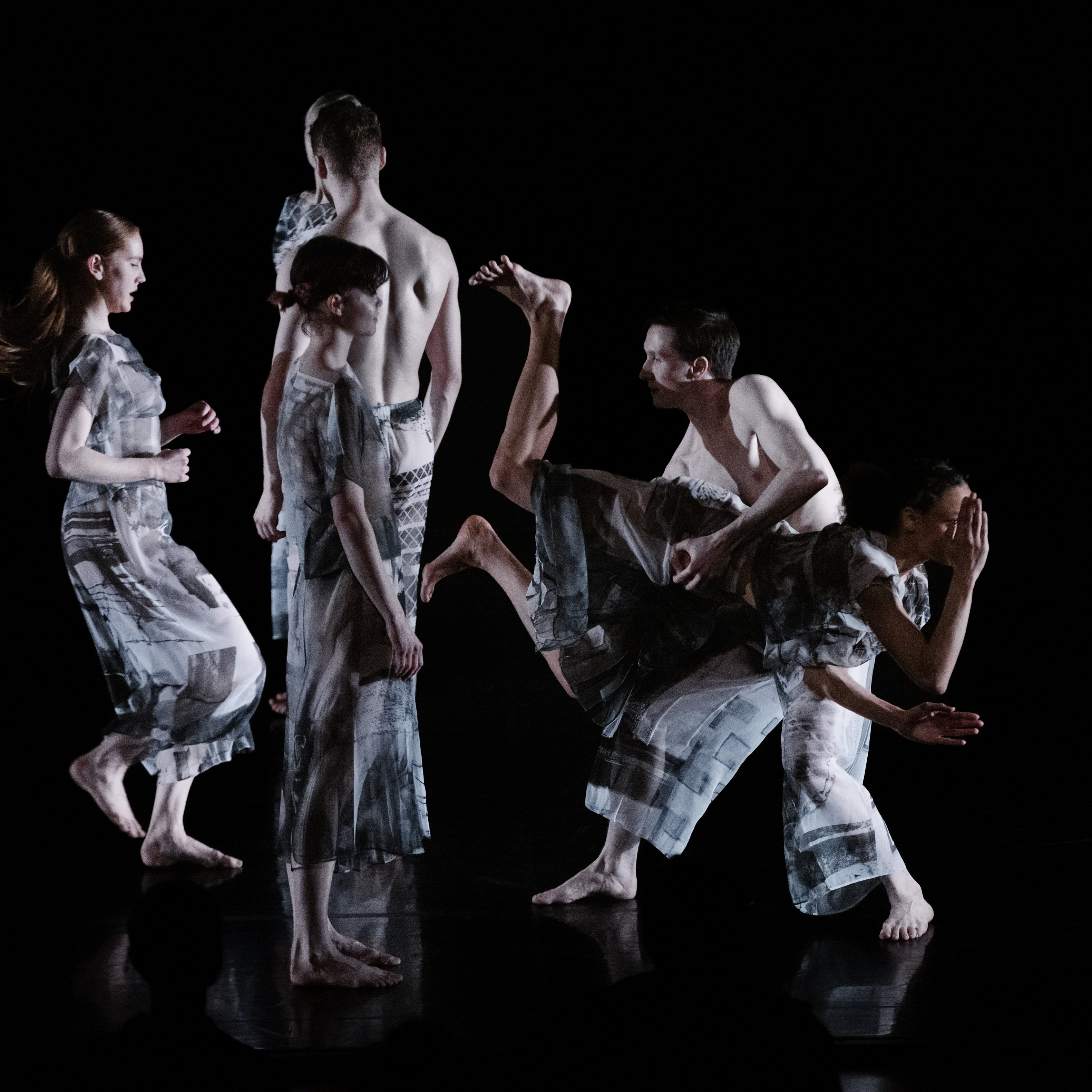 Dancers wearing grey on a dark stage