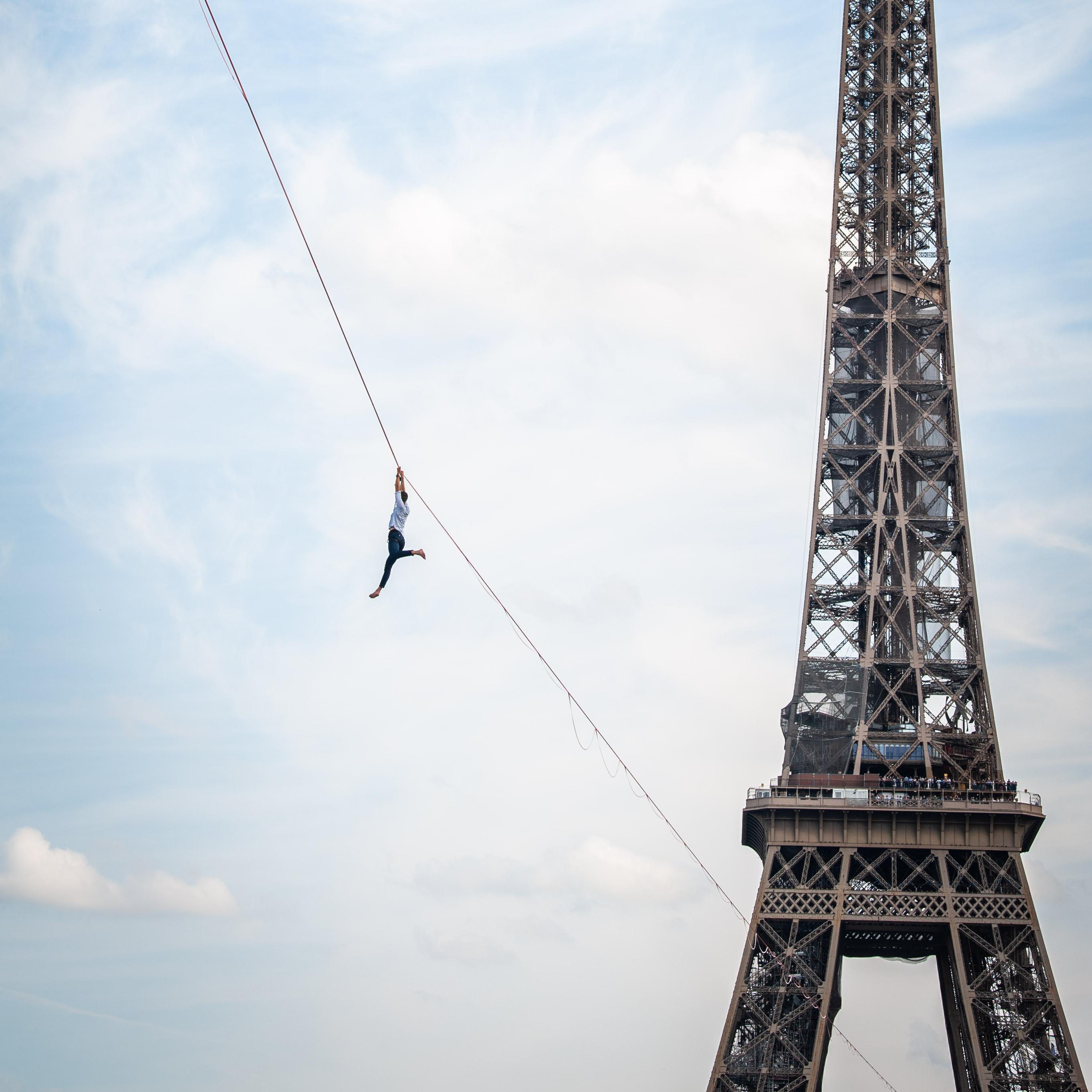 A tightrope walker hanging on a tightrope, next to the Eiffel Tower