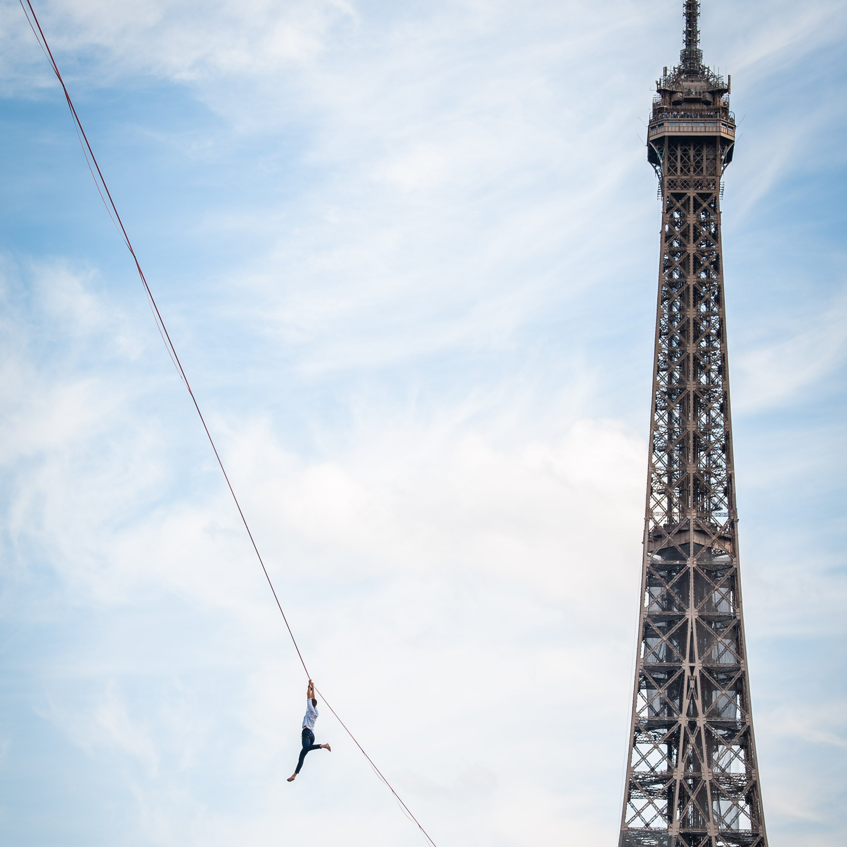 A tightrope walker hanging on a tightrope, next to the Eiffel Tower