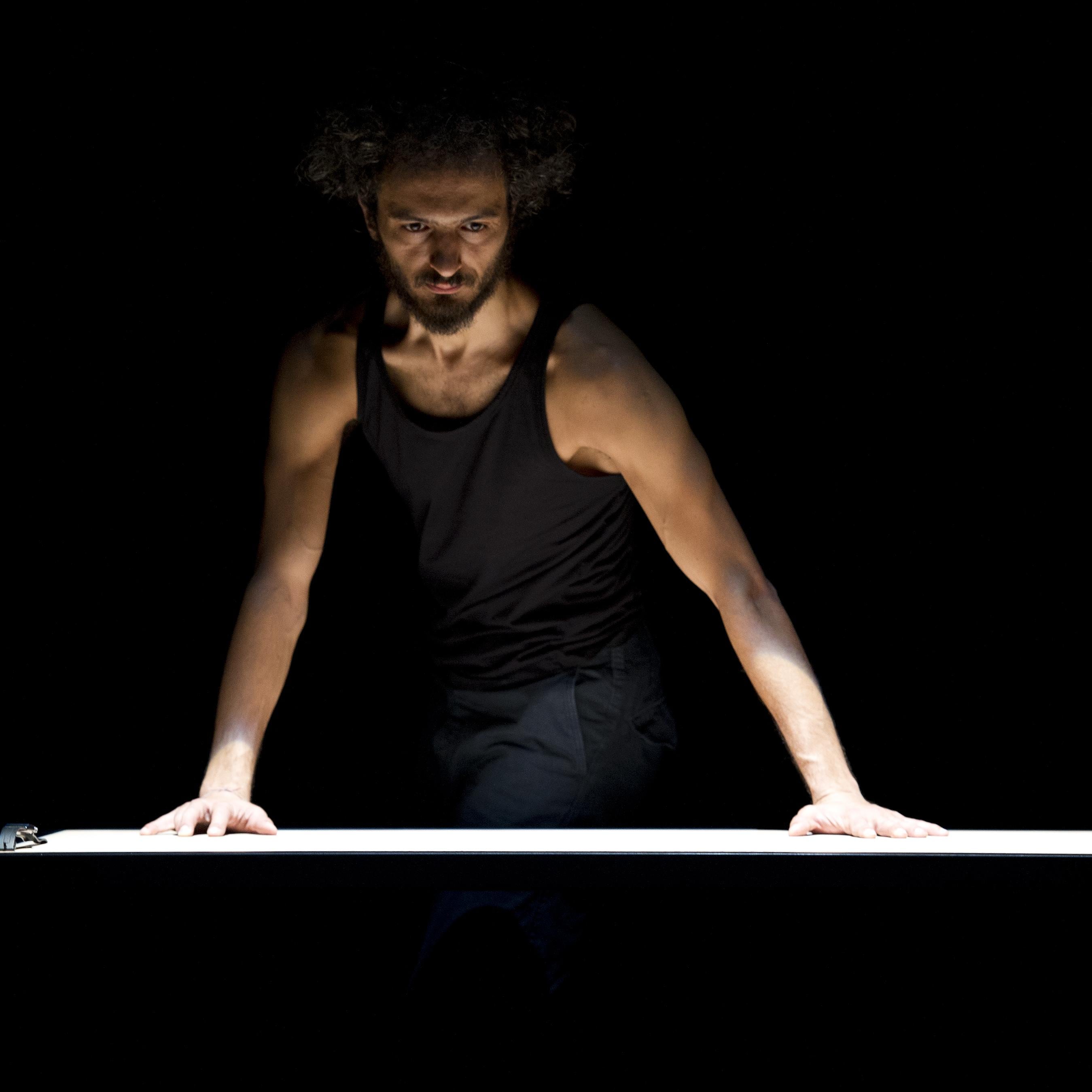 Un homme avec un débardeur noir, ses mains posées sur une table blanche