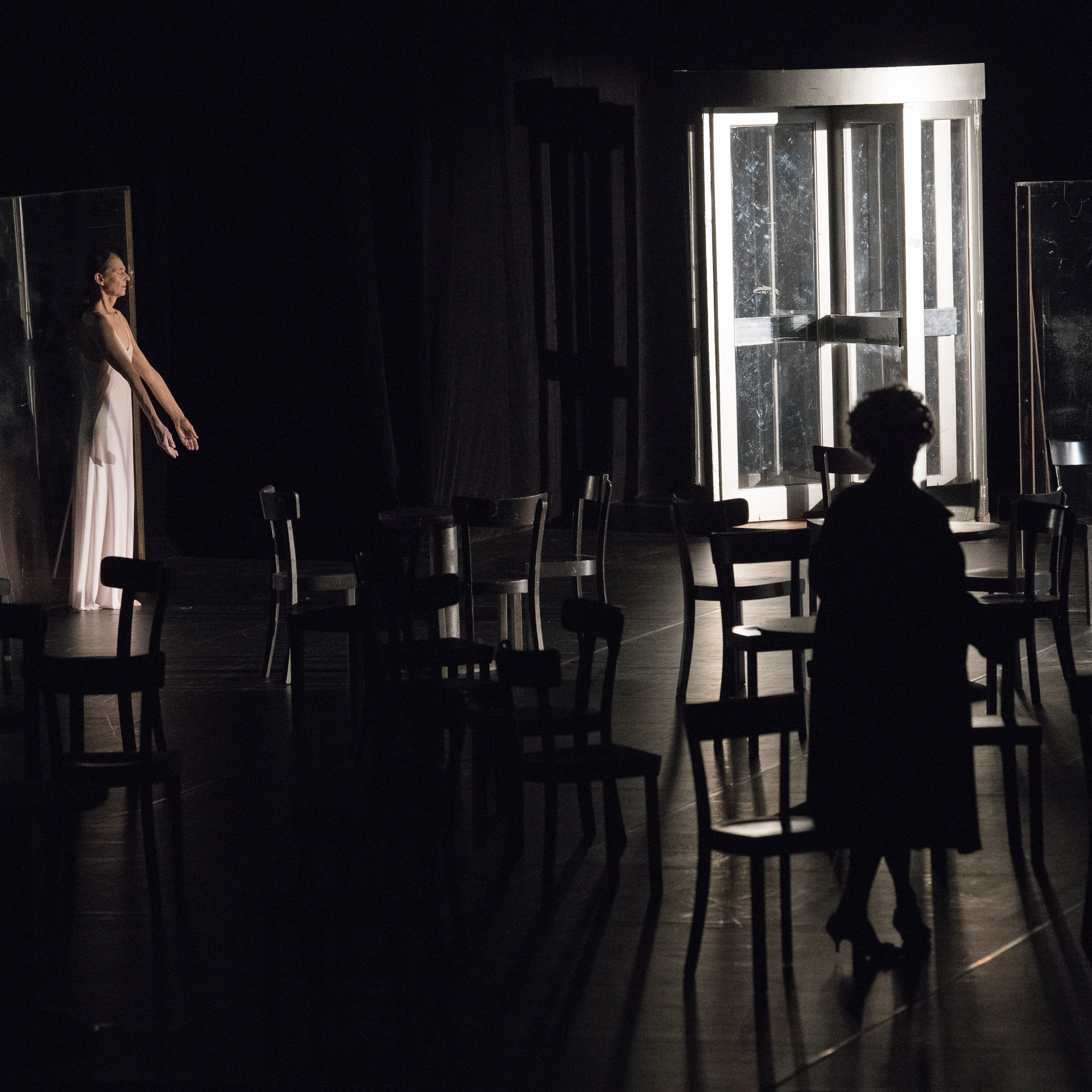 Héléna Pikon is at the back of a stage that is filled with empty chairs, her eyes are closed and her arms stretched downwards.