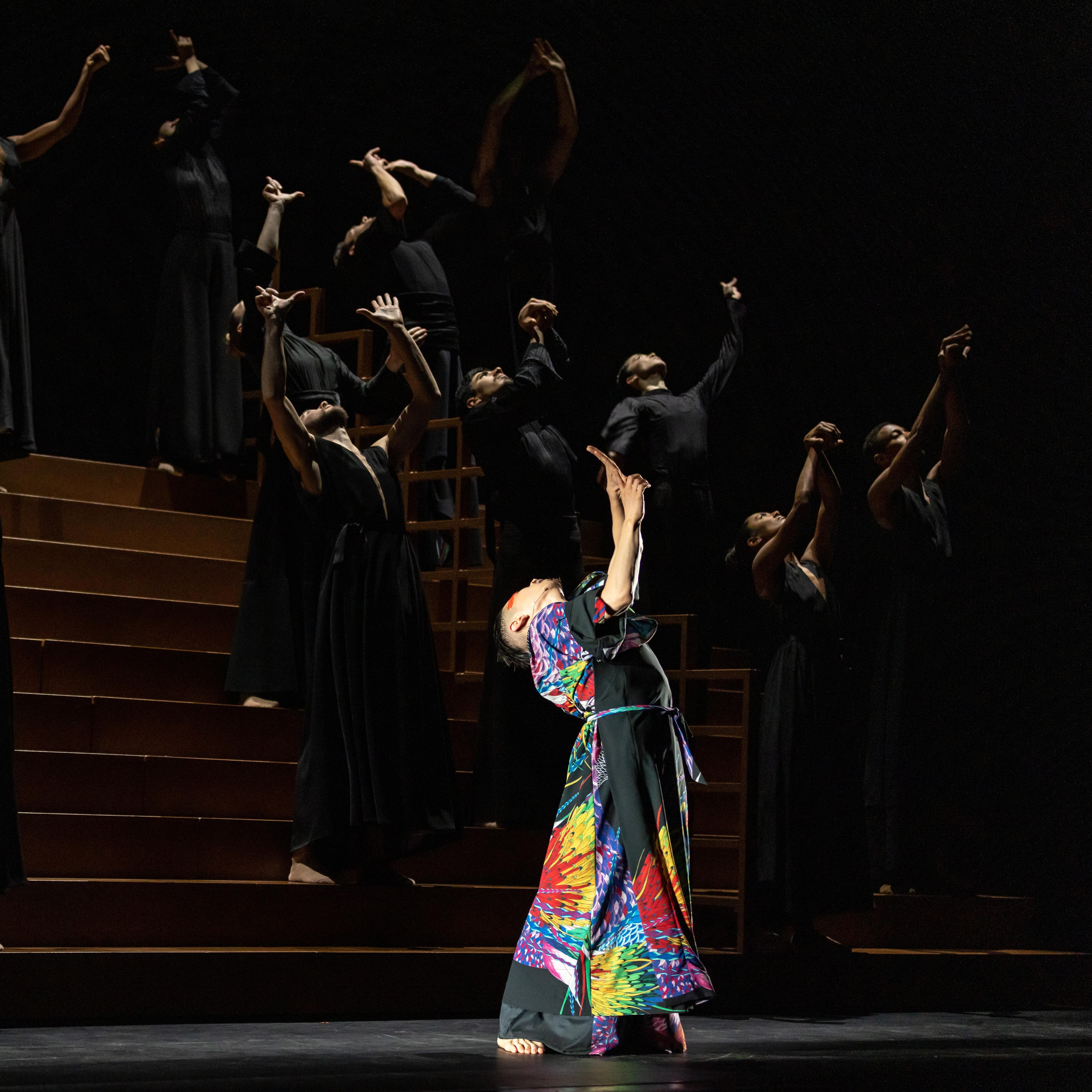 Danseur de Ukiyo-e portant un costume coloré, se penche vers l’arrière les bras vers le haut. Des danseurs en noir font le même mouvement en arrière-plan.