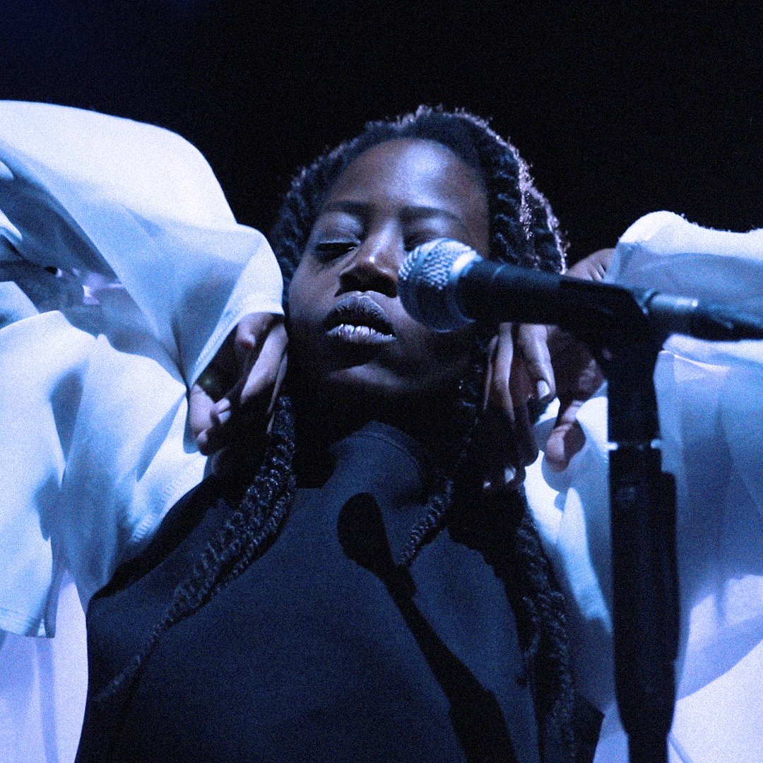 Woman behind a microphone, eyes closed, wearing a white jacket